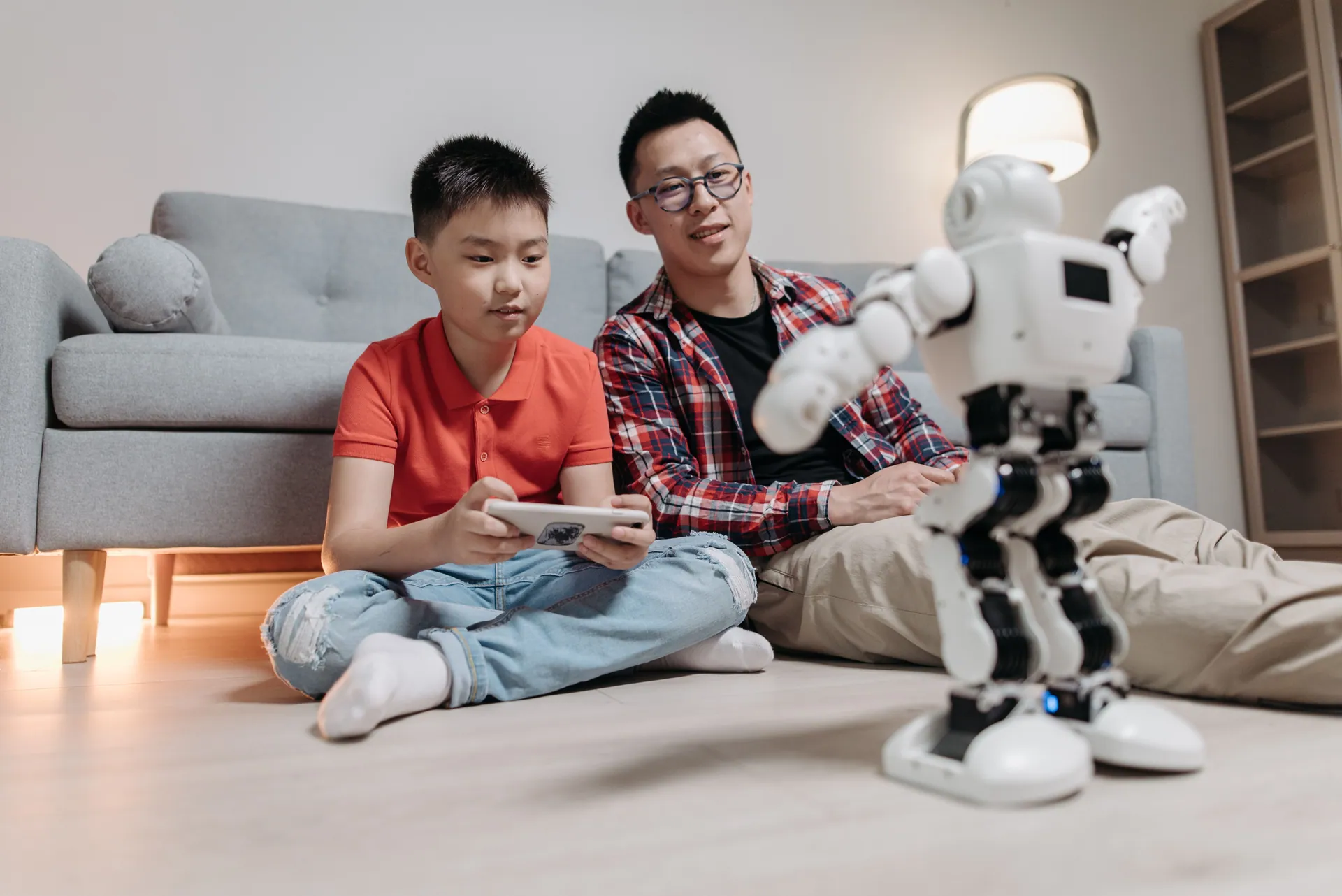A father and his son bonding while playing with a robot and remote control indoors.