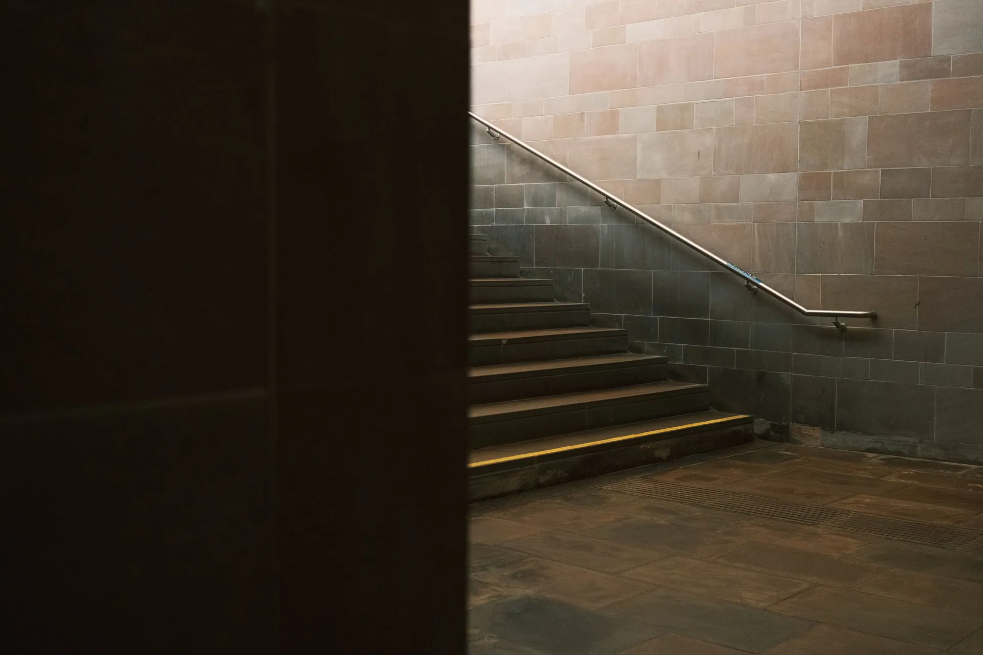 A minimalist staircase with tiled walls and metal railing in a dimly lit indoor setting.