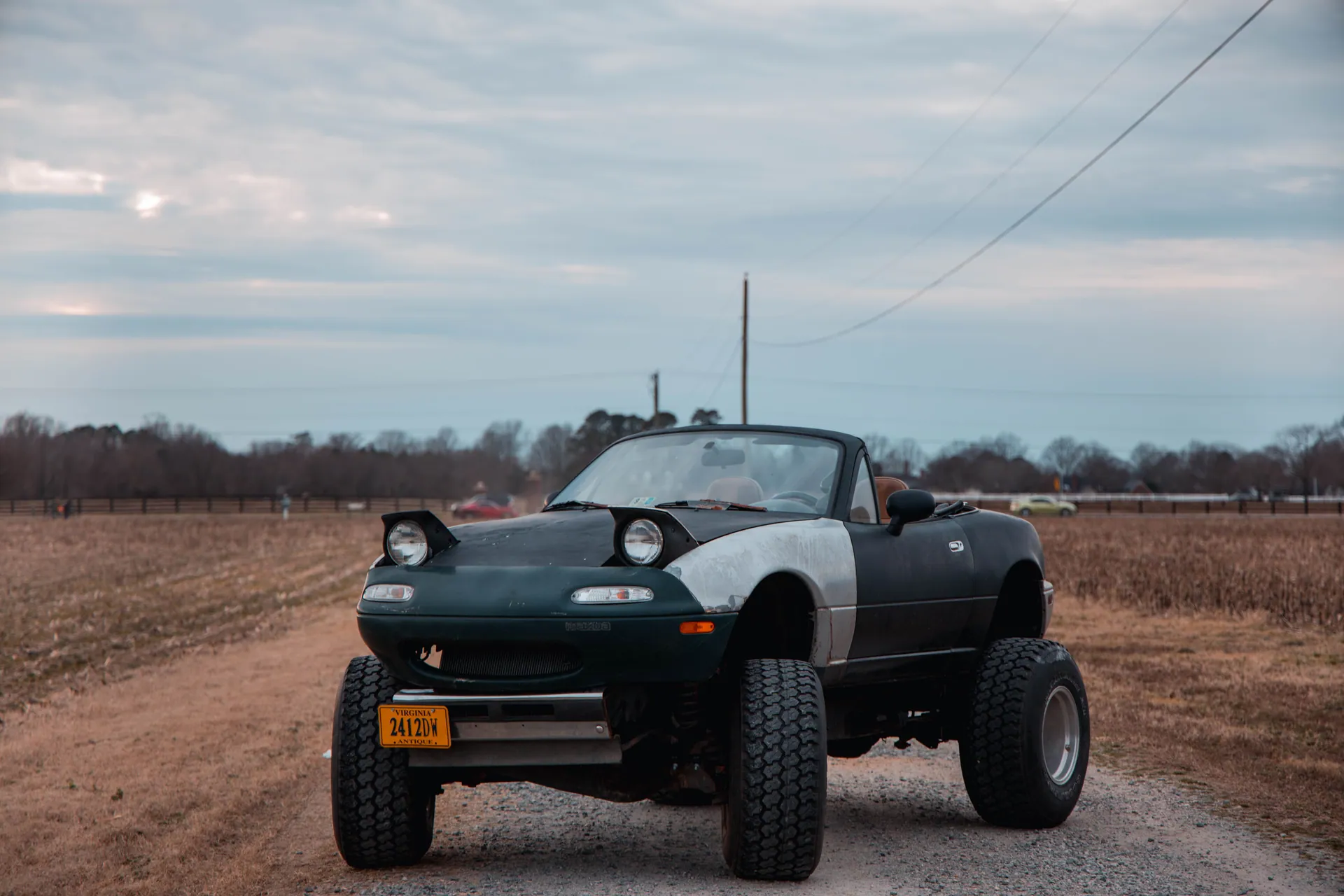 A modified convertible car with large tires on a rural dirt road, ready for off-road adventures.