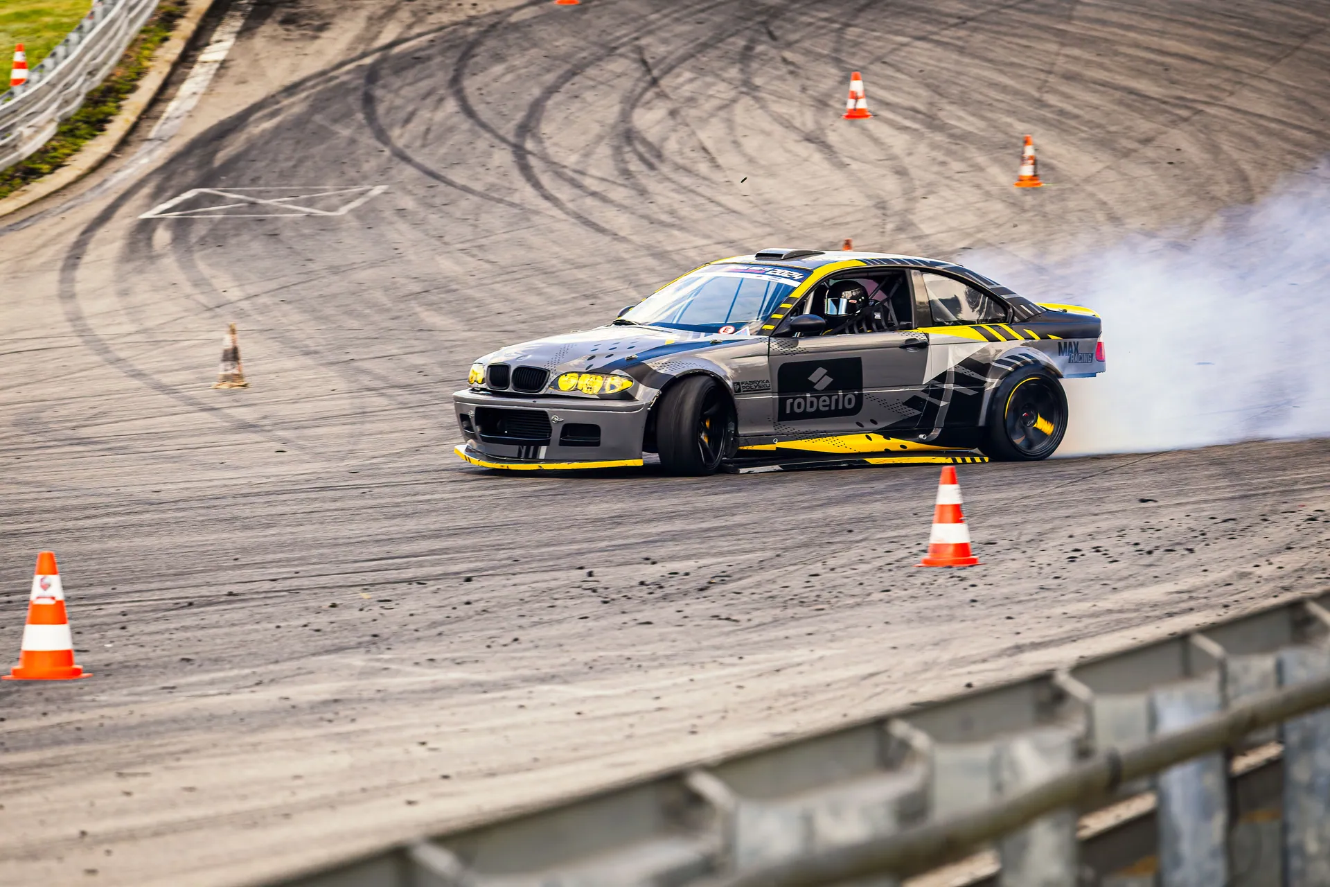 A dynamic drift car maneuvering on a race track with smoke and cones.