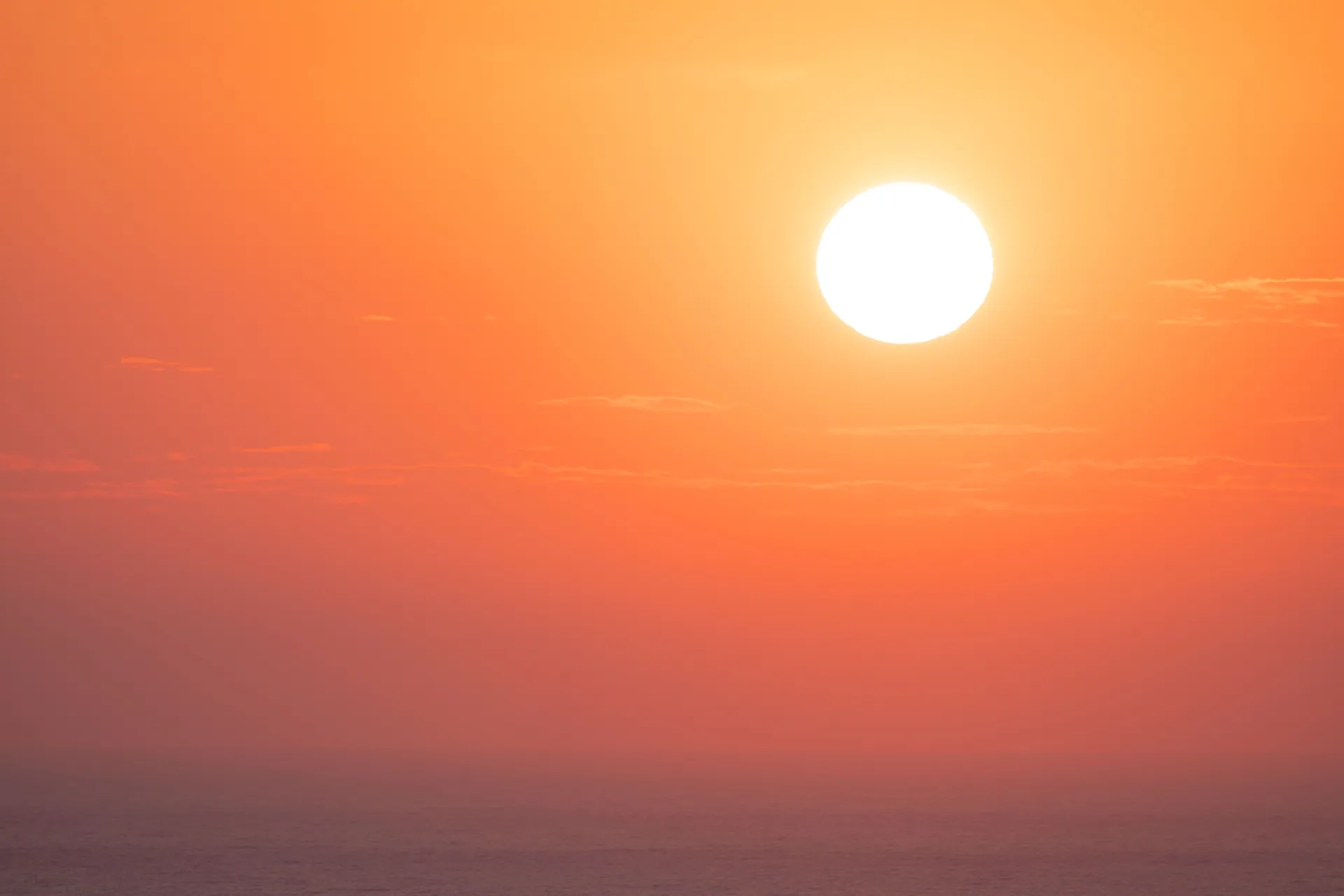 A vibrant sunset casts warm orange hues over a calm ocean, creating a serene and peaceful ambiance.
