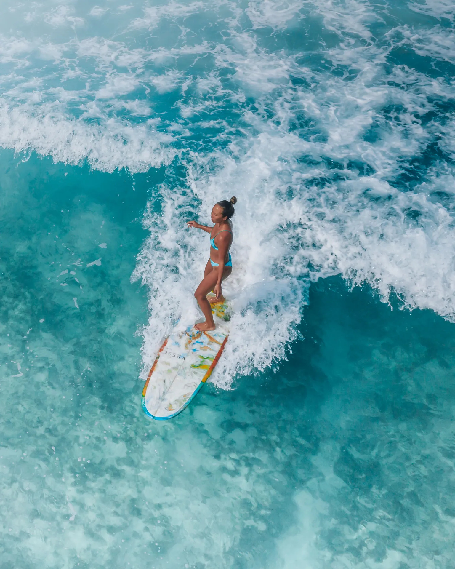 Stunning aerial shot of a woman surfing a blue ocean wave, capturing the thrill of water sports.