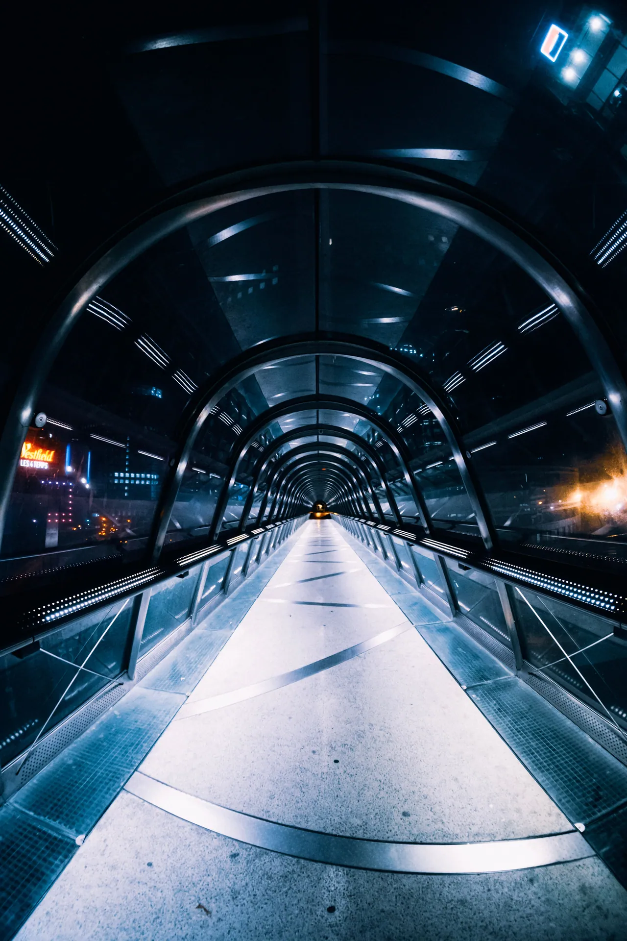 A futuristic pedestrian overpass tunnel illuminated at night with modern architectural design.