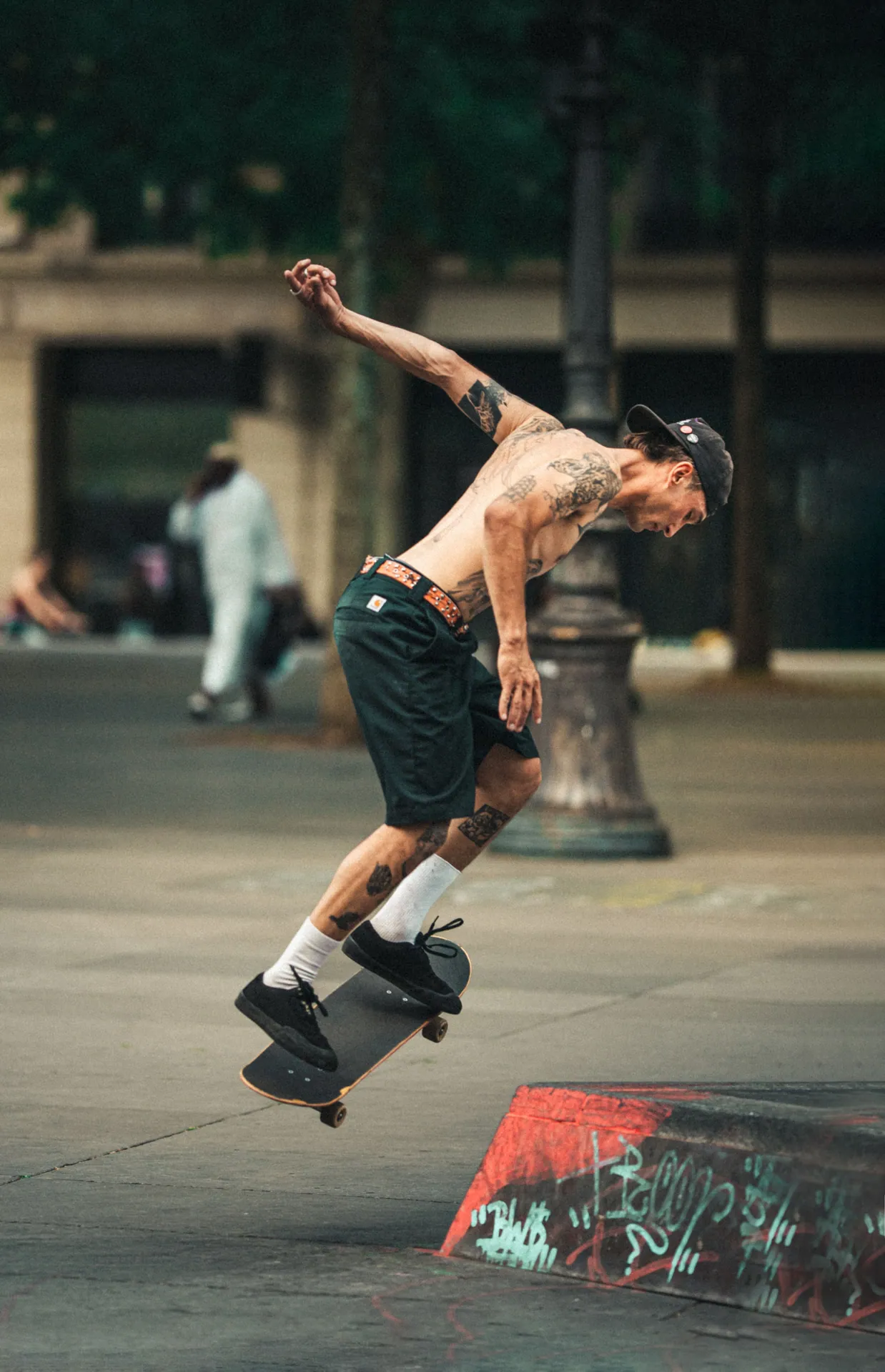 Tattooed skateboarder doing a trick on the street with blurred background.