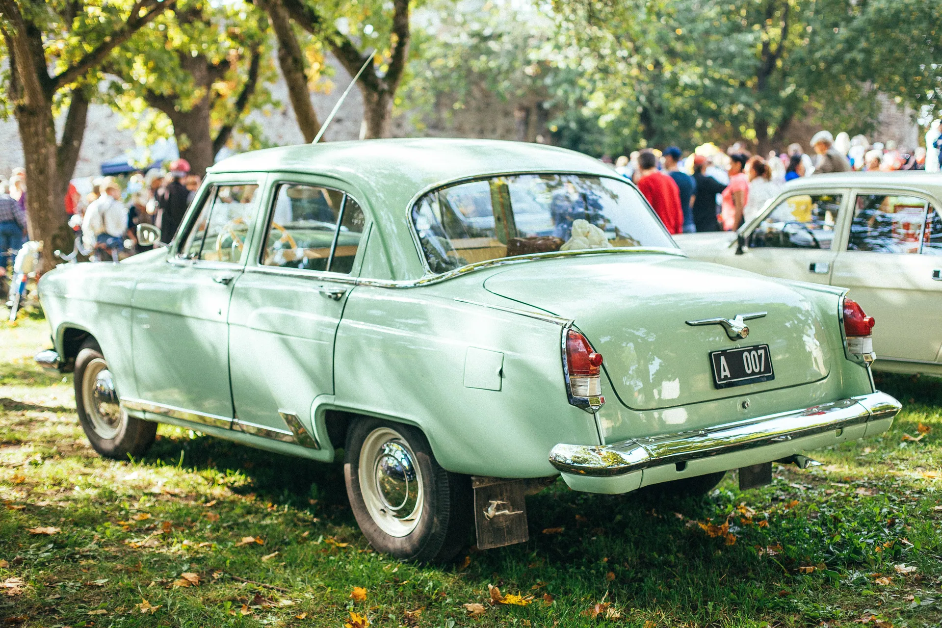 A retro green car parked under trees at an outdoor car show event.
