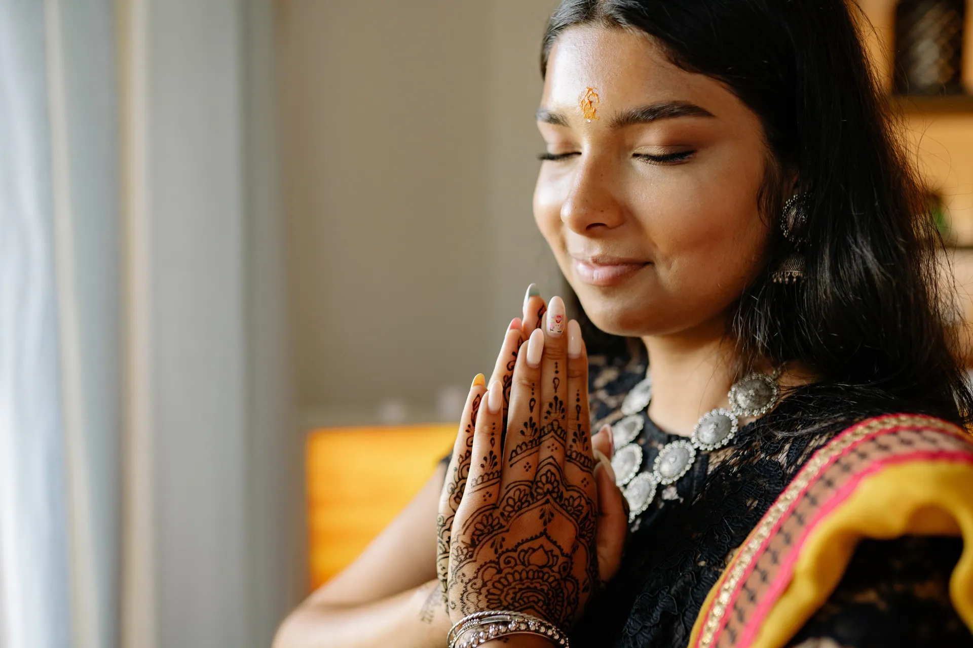 A woman in traditional Indian attire prays during Diwali, showcasing intricate henna designs.