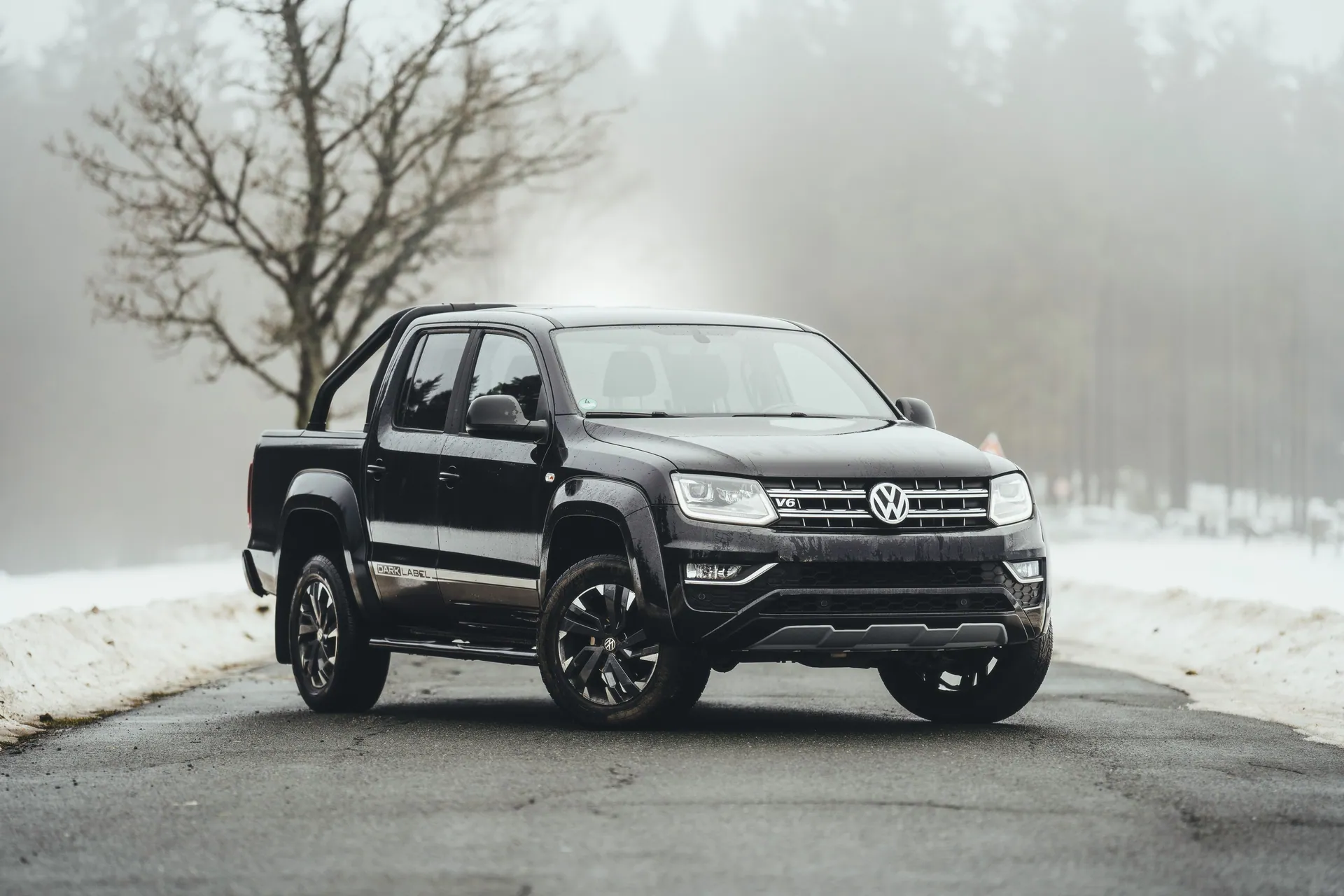 Black Volkswagen pickup truck on a snowy rural road with foggy winter trees.