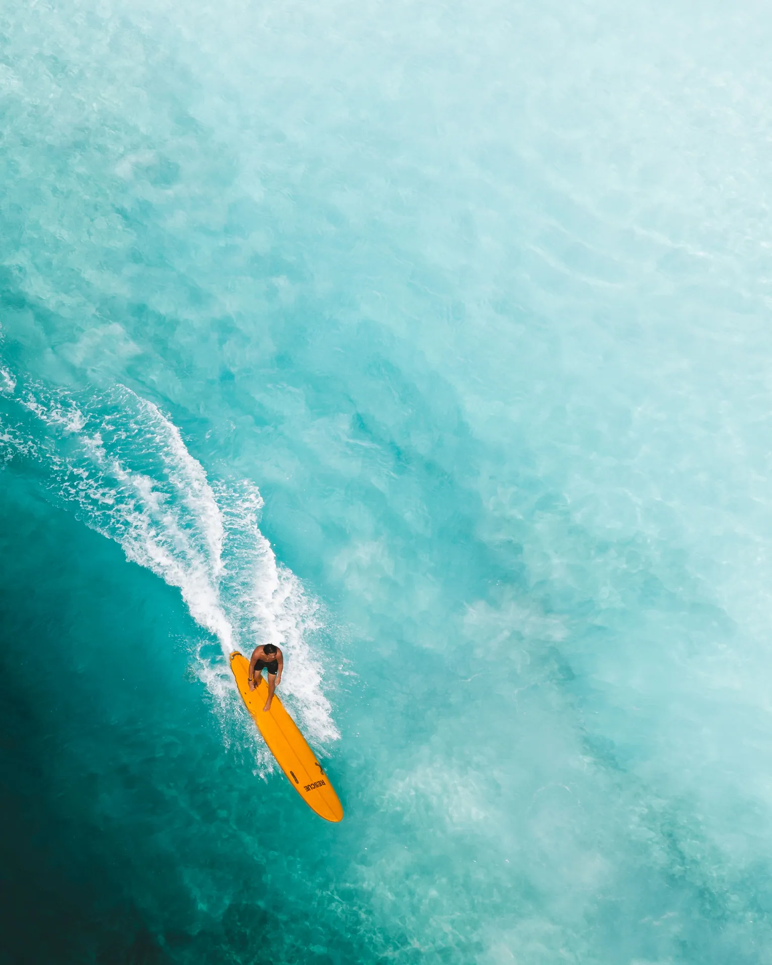 Dynamic aerial shot of a surfer on a yellow board cutting through a turquoise wave, capturing the essence of ocean adventure.