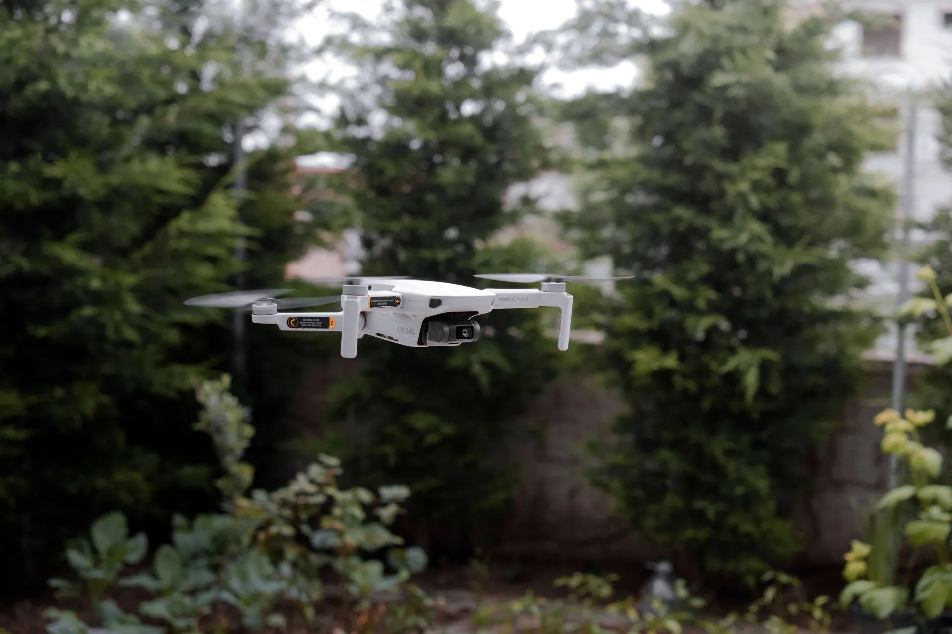 Close-up of a white drone flying outdoors with green foliage in the background.