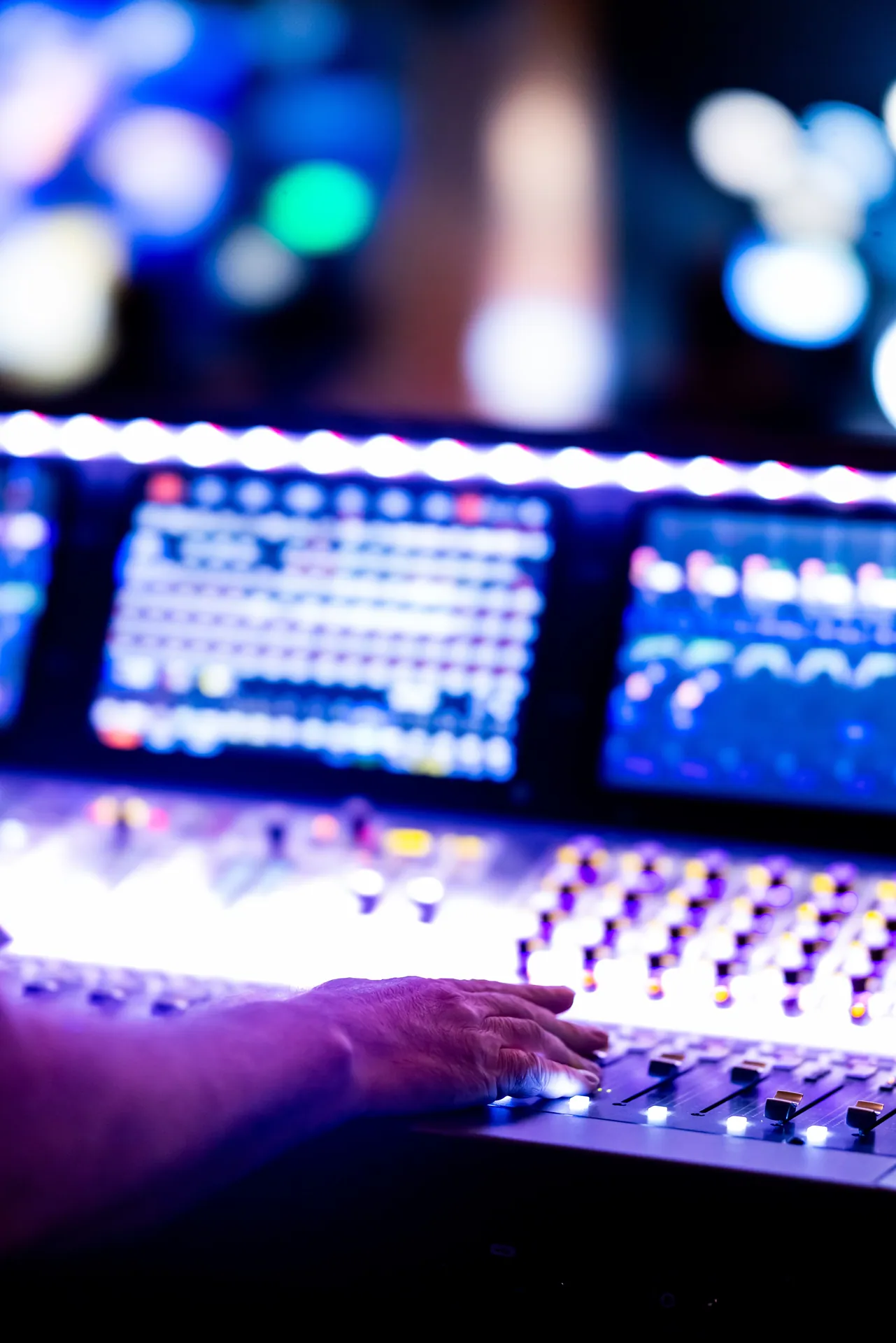 Close-up of a hand operating an audio mixing console with colorful LED lights in a studio setting.