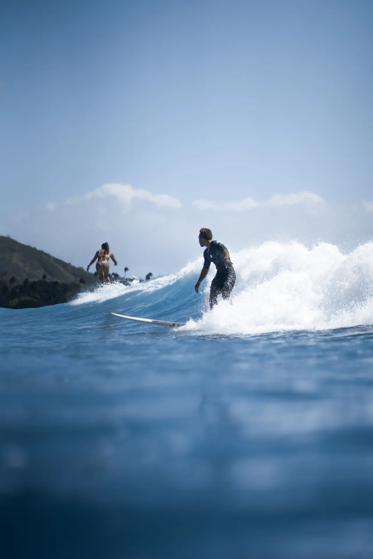 Group of surfers balancing on board while catching splashing wave in sunny day