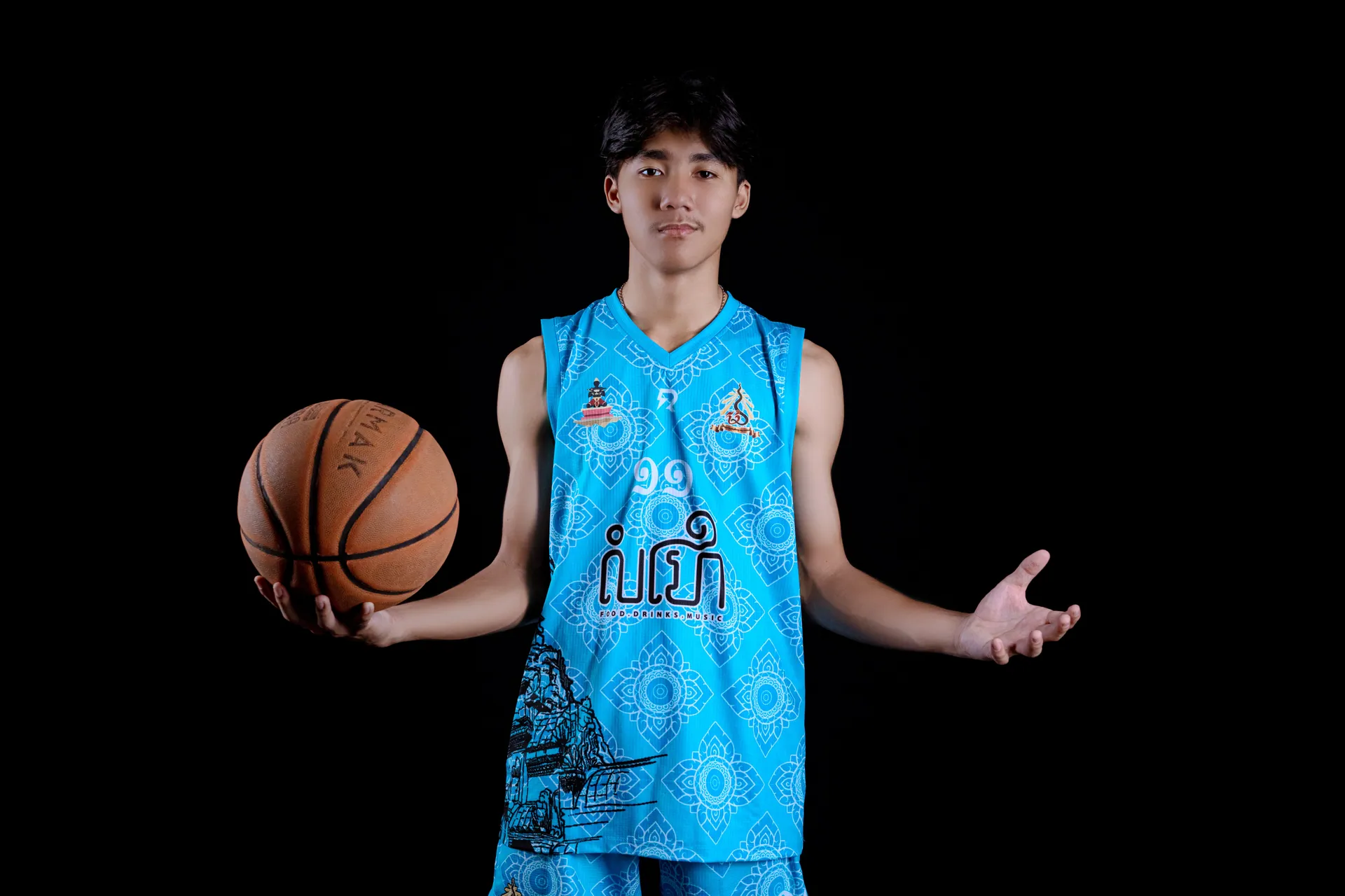 Teenager holding basketball in blue jersey against a black background, symbolizing youth sports and athleticism.