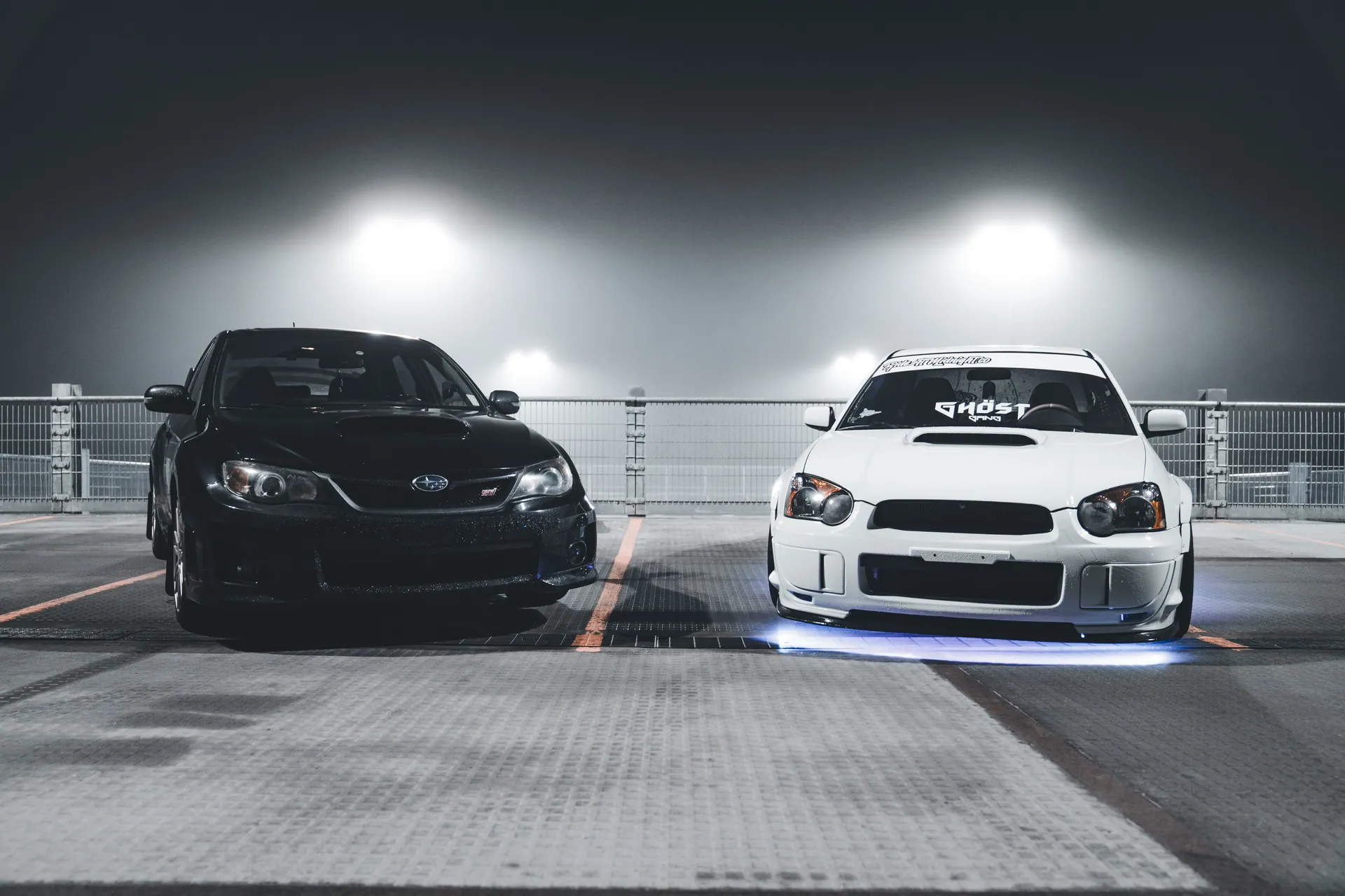 Twin custom Subaru WRX cars with standout features parked at night in an urban setting.