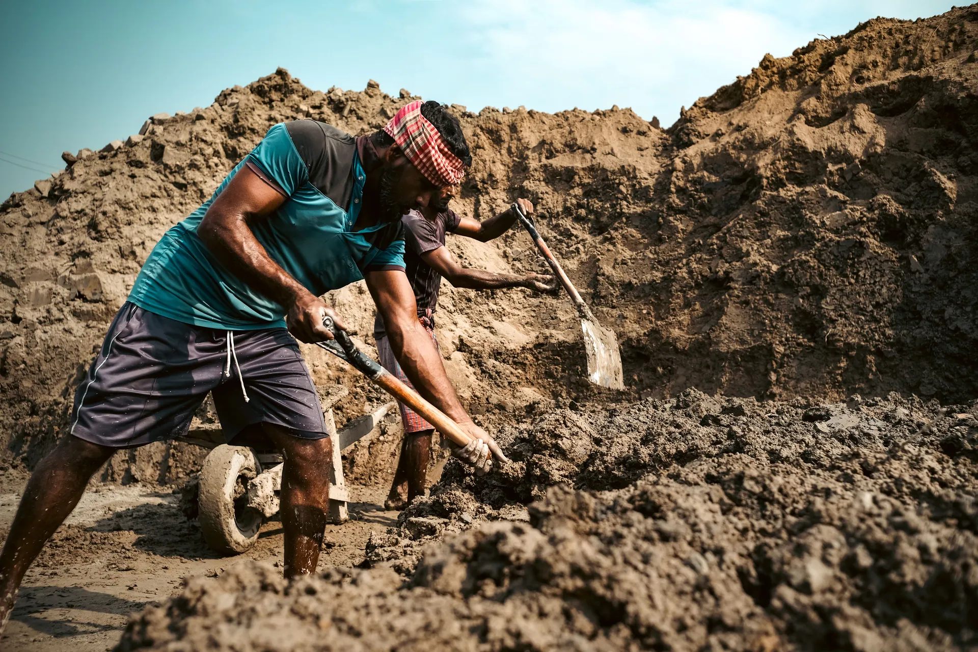 Two workers engaged in intensive digging at a construction site under blue skies.