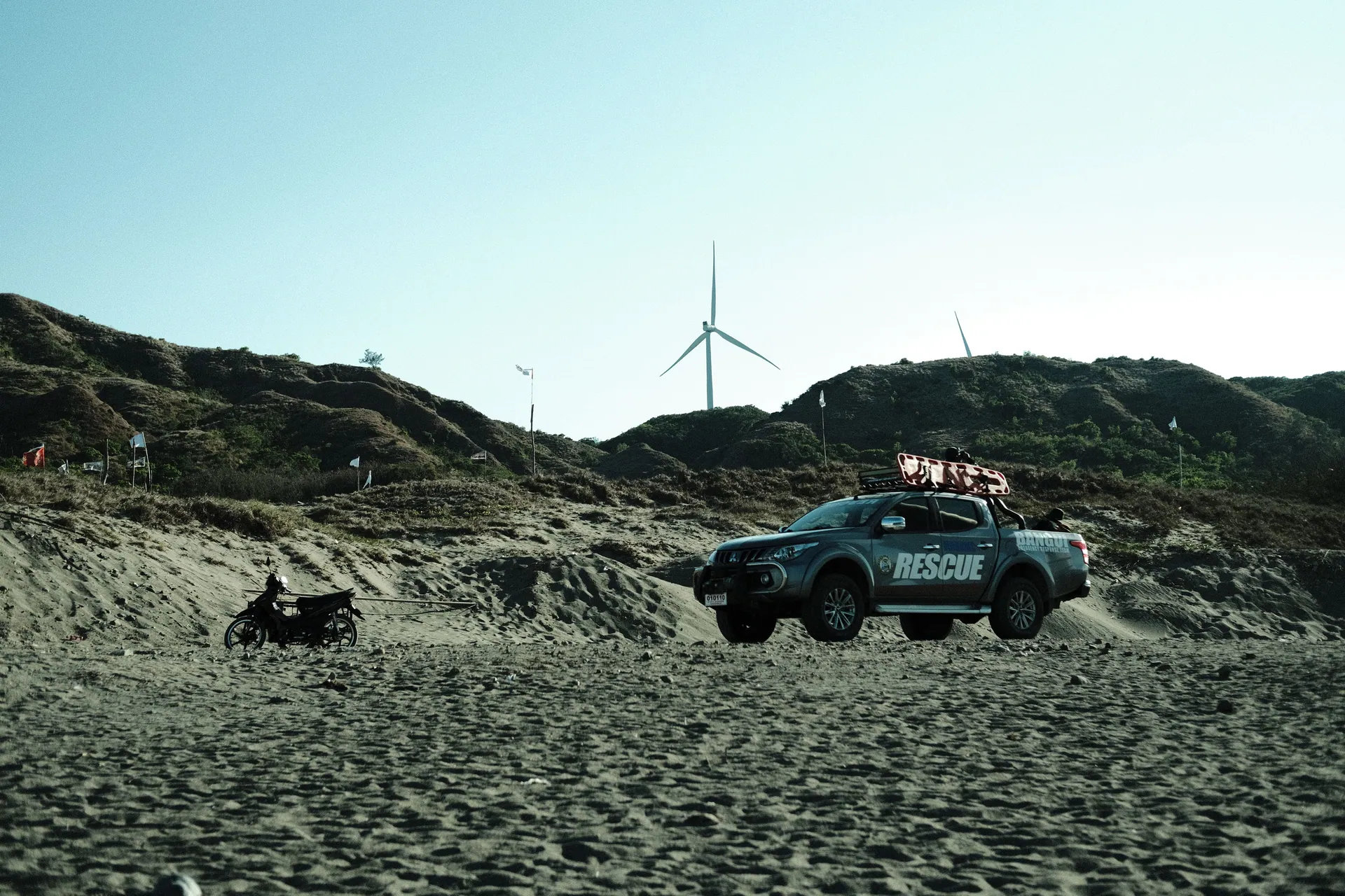 A rescue truck traversing sandy terrain with wind turbines in the background.