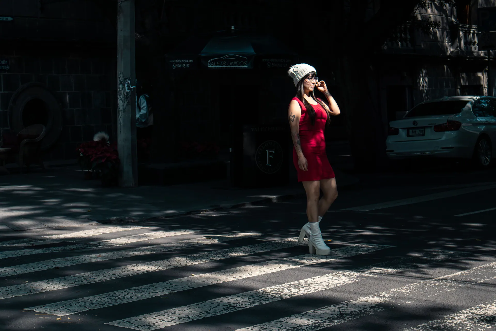 Fashionable woman in red dress crossing a street in an urban setting.