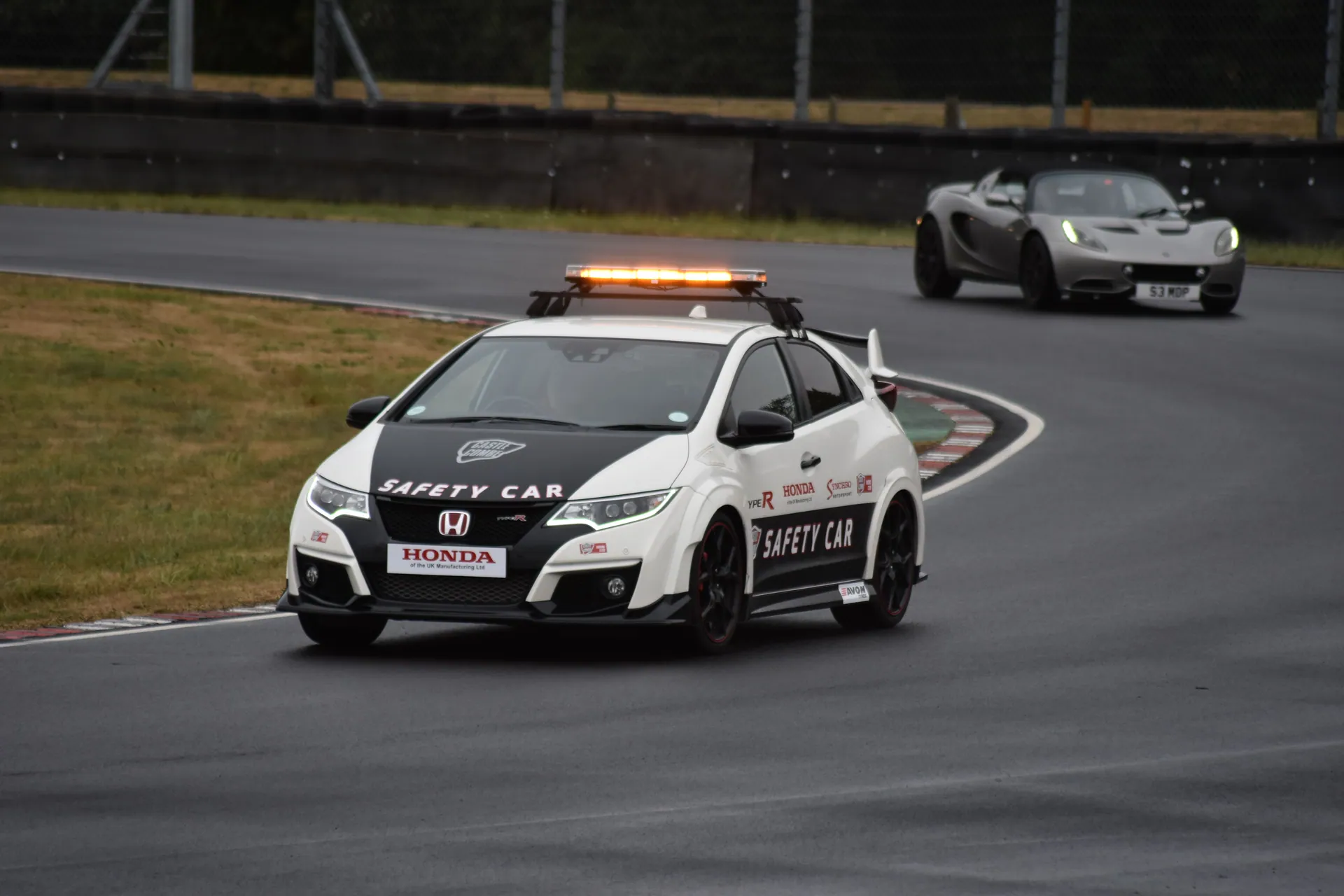 Safety car leading a convertible on a wet race track during a curve.