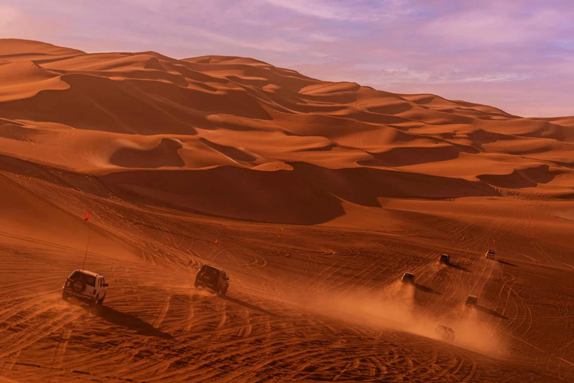 Off-road SUVs kick up dust in a dramatic desert landscape at sunset, capturing the thrill of adventure.