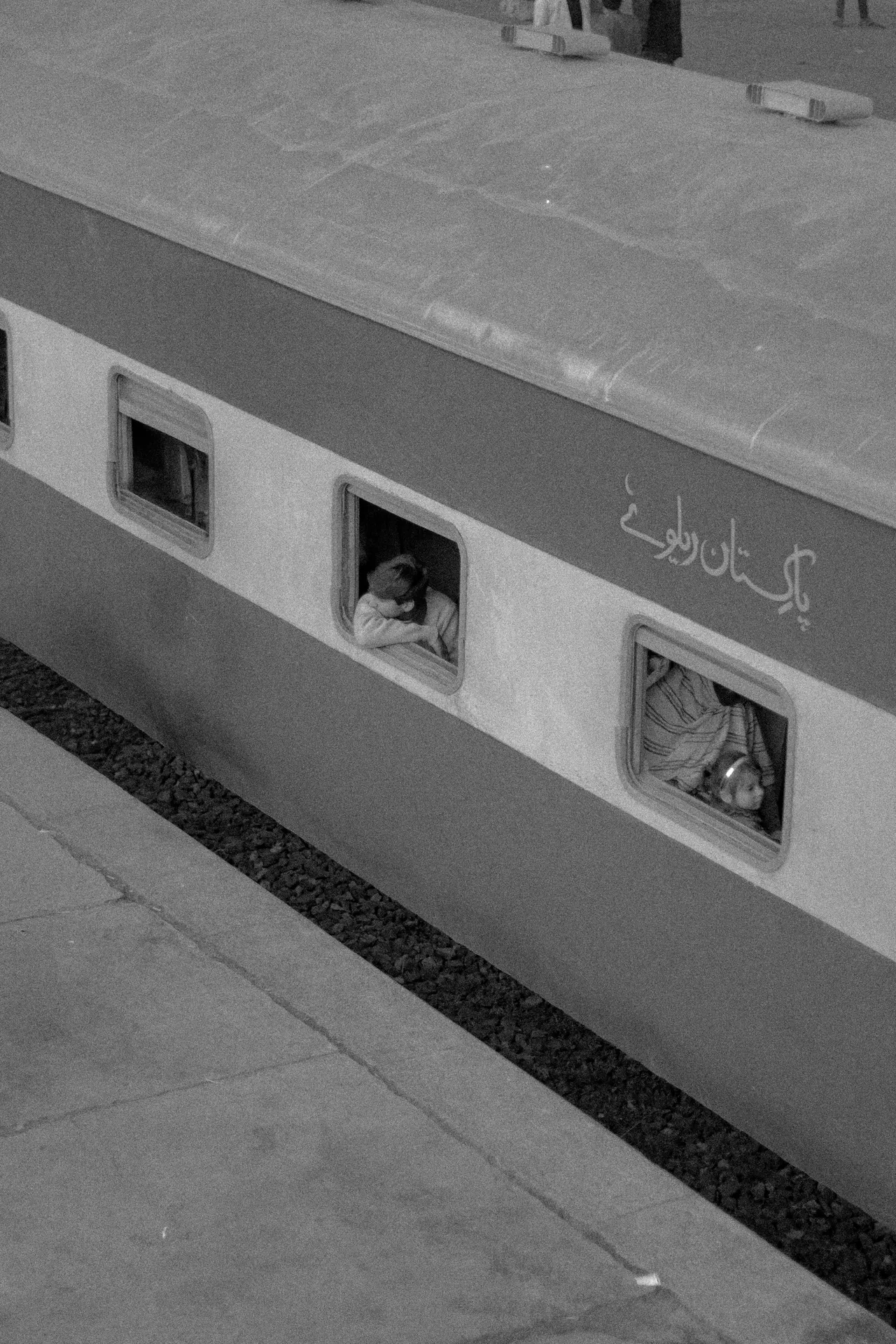Vintage black and white photo of a Pakistani train with passengers peeking out, capturing a moment in time.