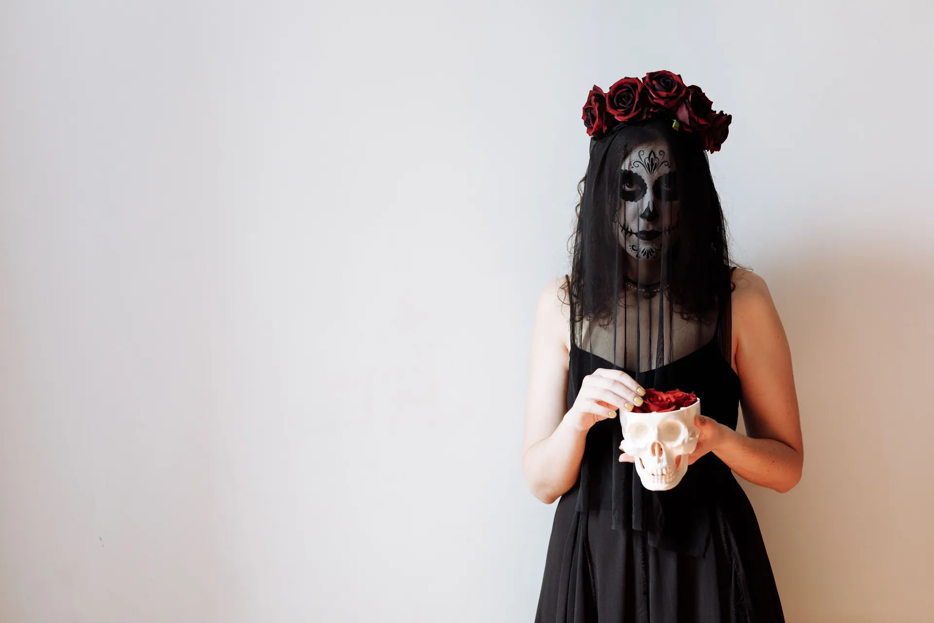 Woman with Dia de los Muertos makeup holding a skull, wearing a black veil and red roses.