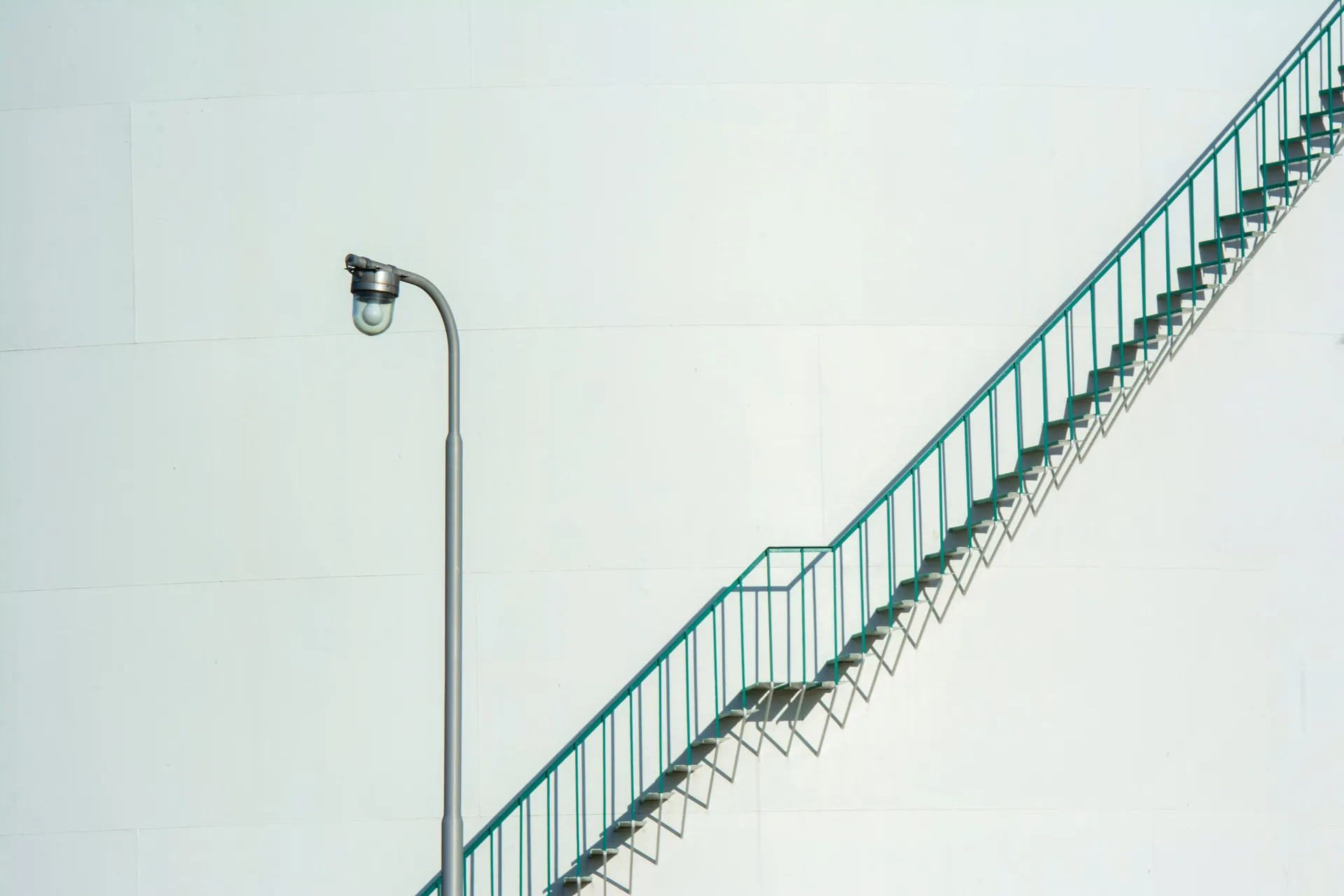 A minimalist view of an industrial staircase and street light against a white backdrop.