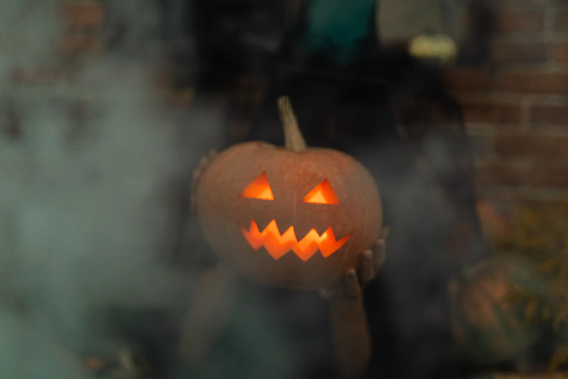 A glowing jack-o'-lantern held in hands surrounded by eerie smoke, perfect for Halloween.
