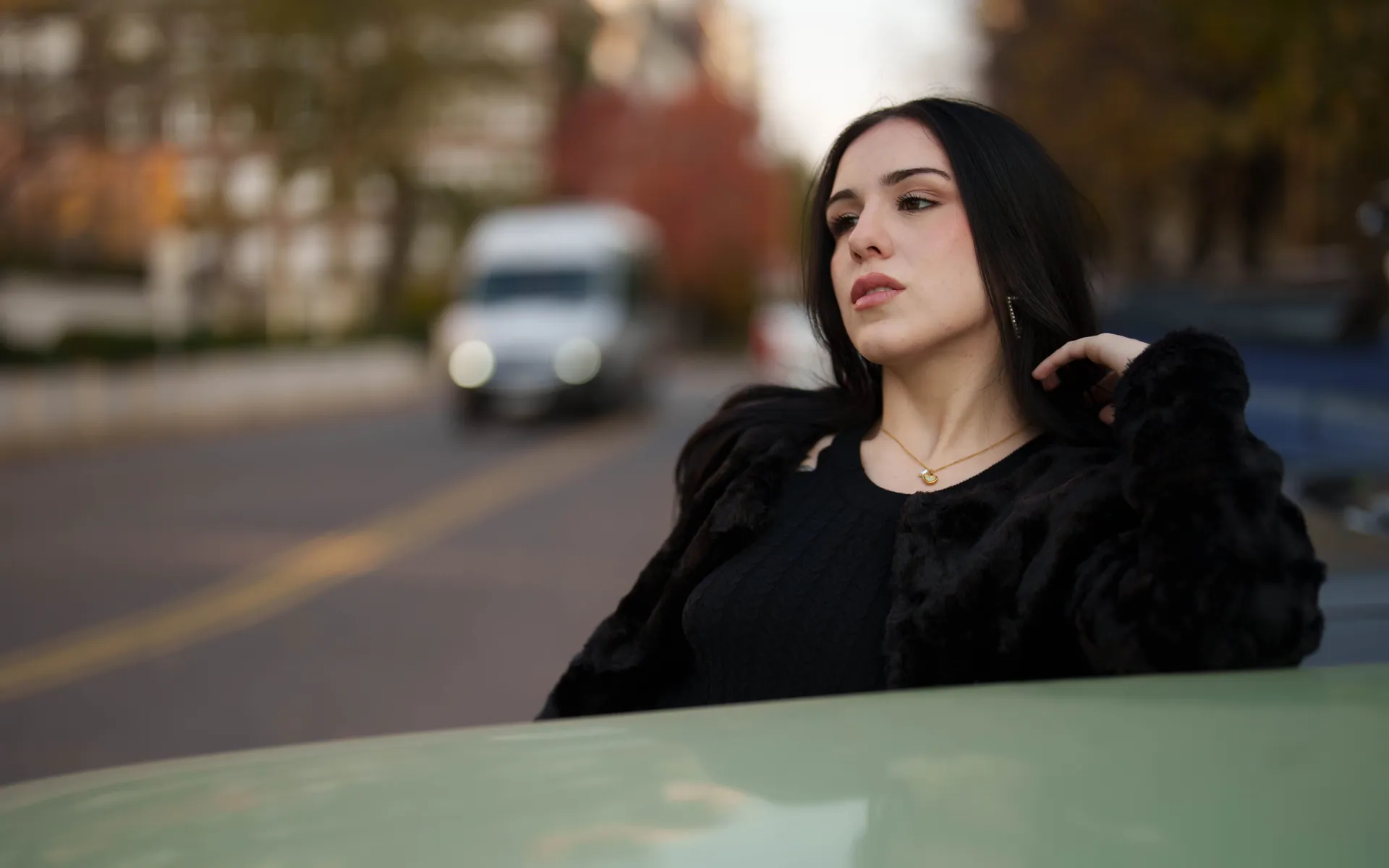 Stylish young woman posing next to a road in a city with blurred background.