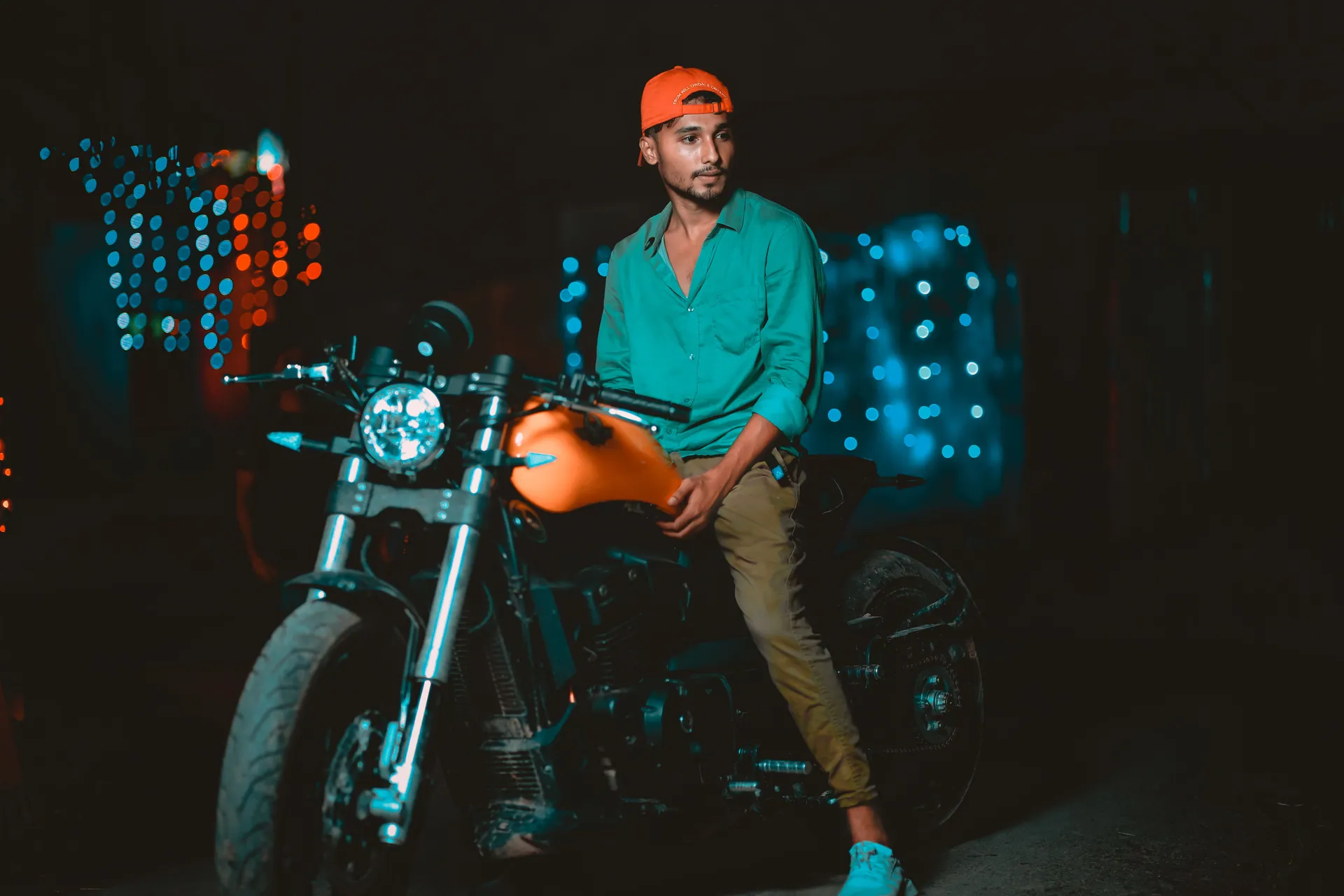 A young man in a red cap sits on a motorcycle at night in Chittagong.