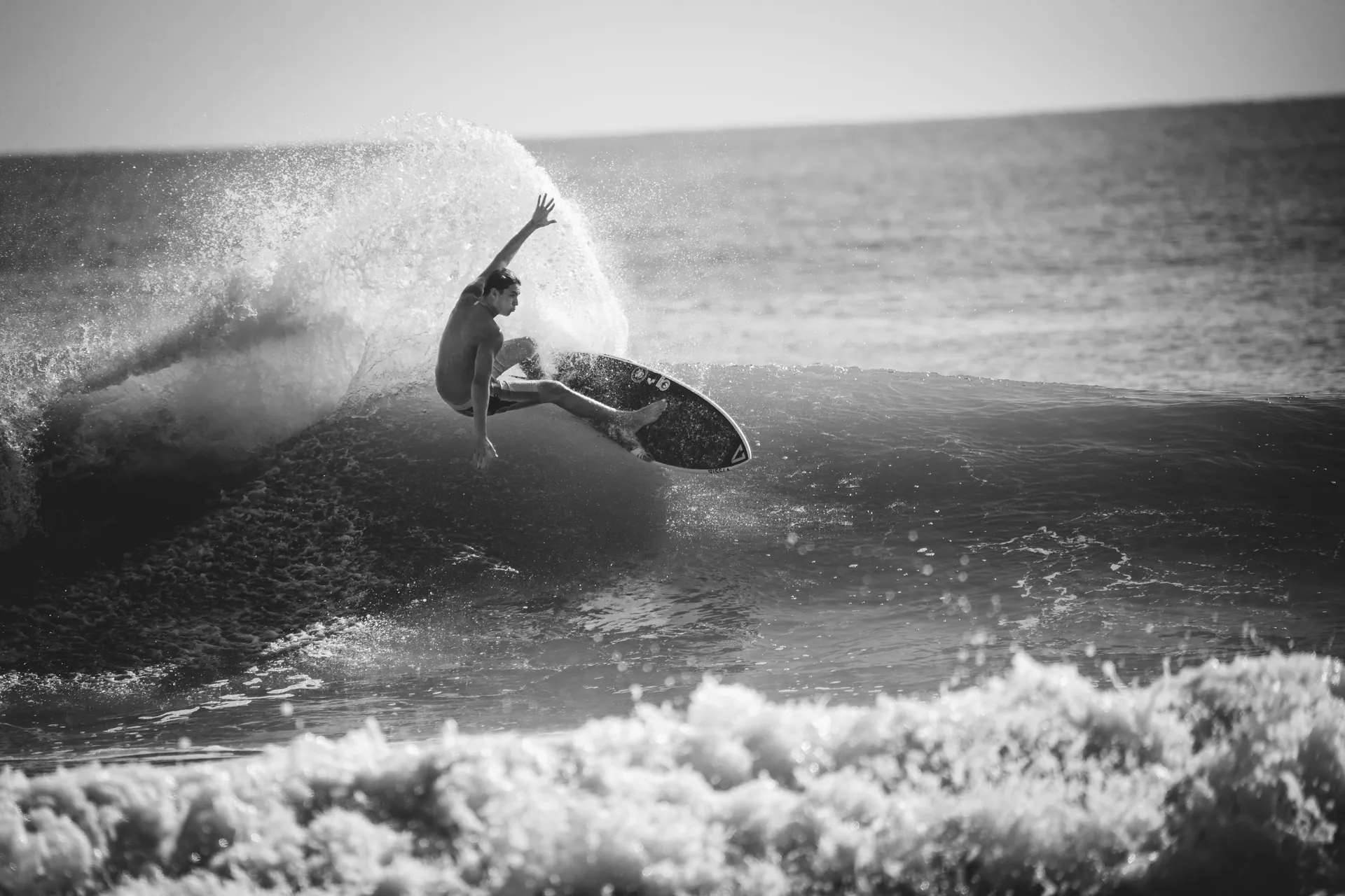 A surfer skillfully rides a wave in an exciting black and white action shot.