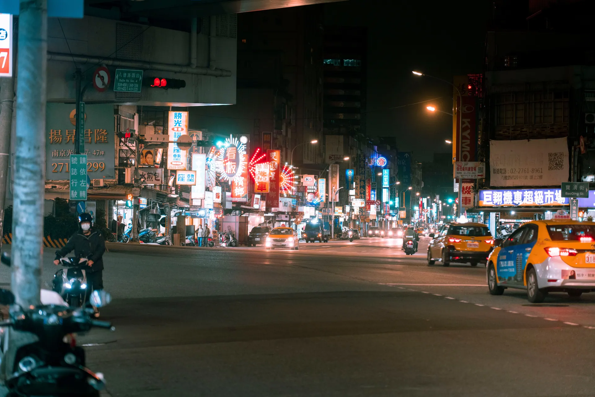 Bustling nighttime city street with glowing neon signs and moving traffic.