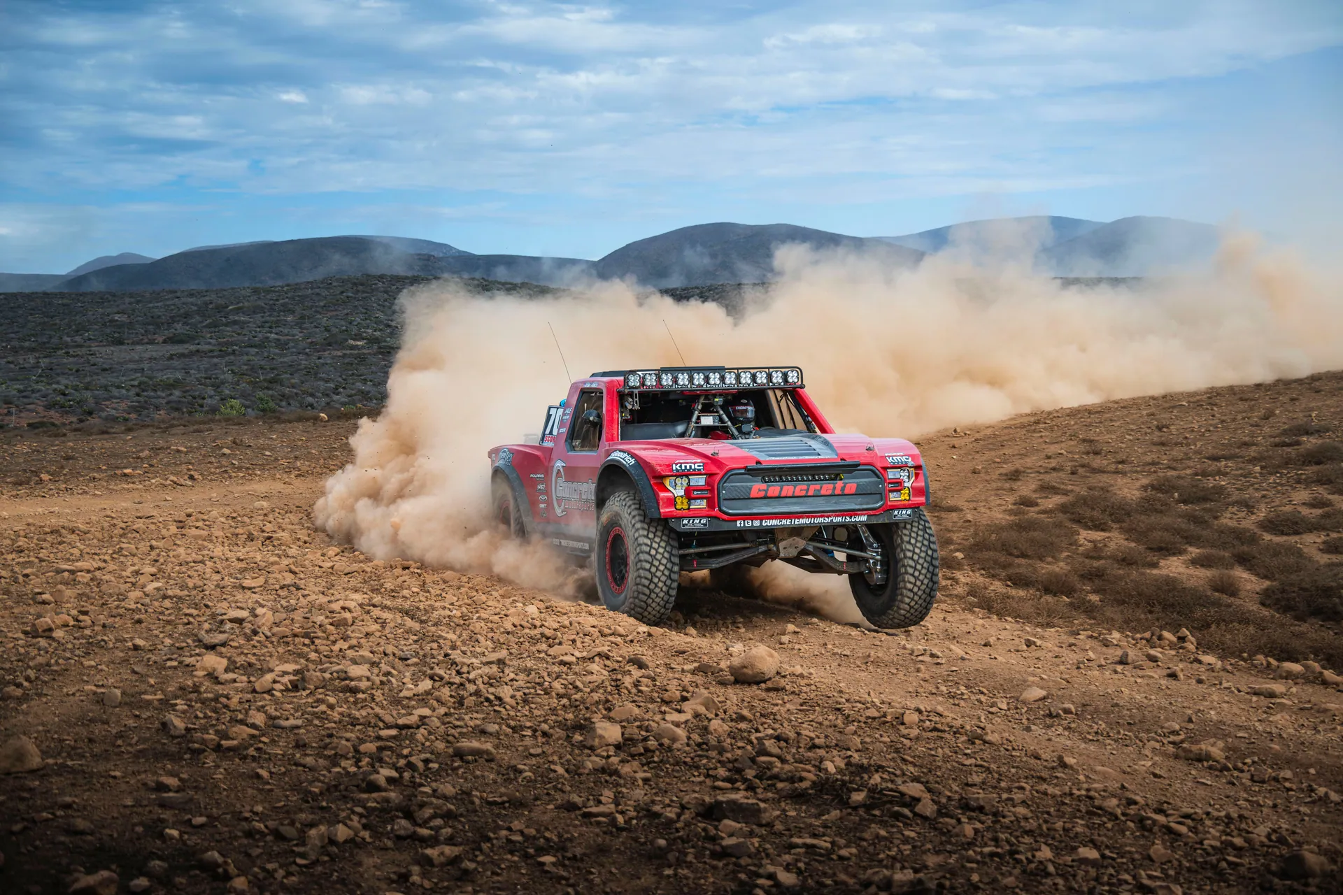 A powerful truck competes in a thrilling off-road race through the rugged Baja desert, kicking up dust.