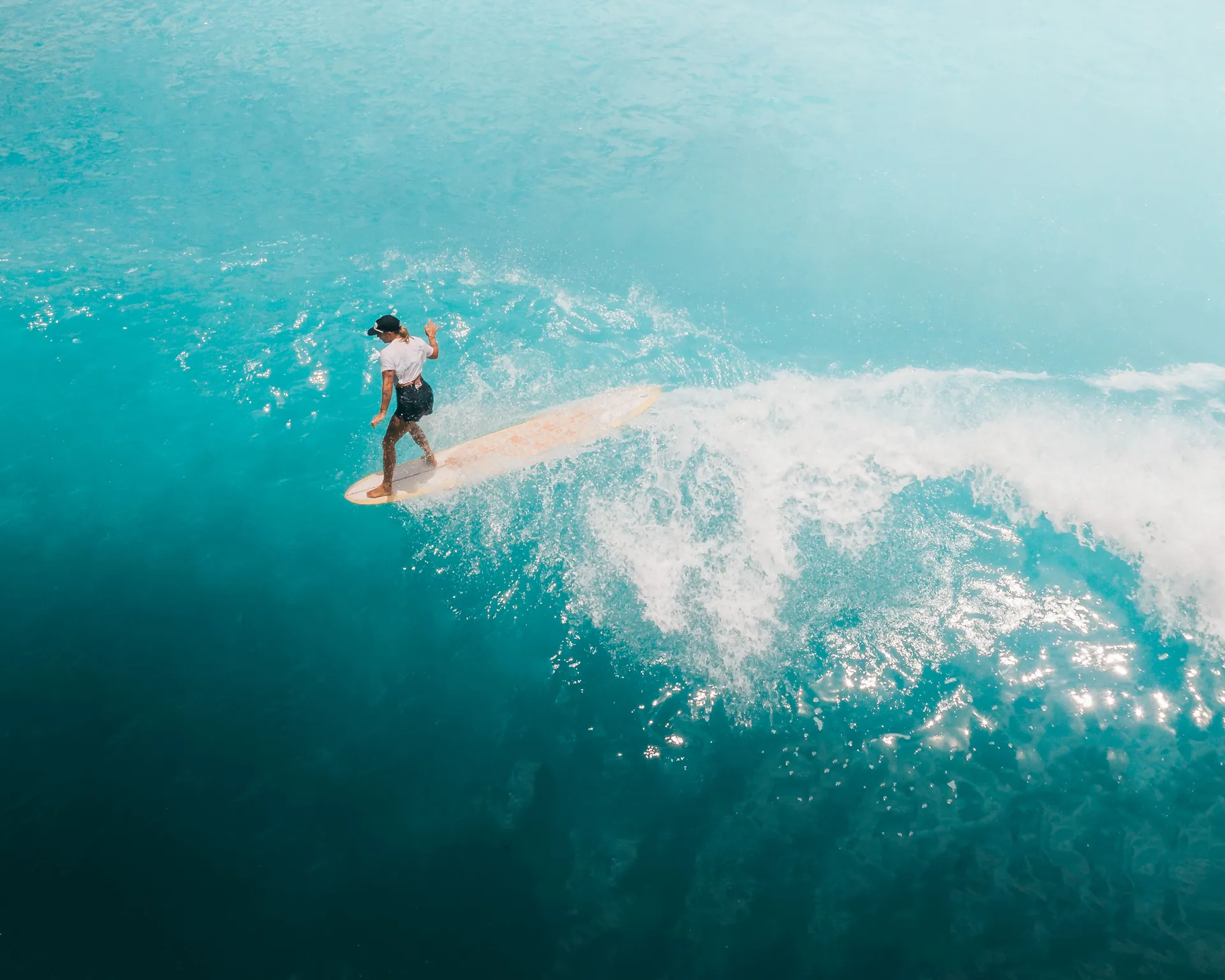 High-angle shot of a woman surfing on a vibrant blue ocean wave, showcasing dynamic water action.