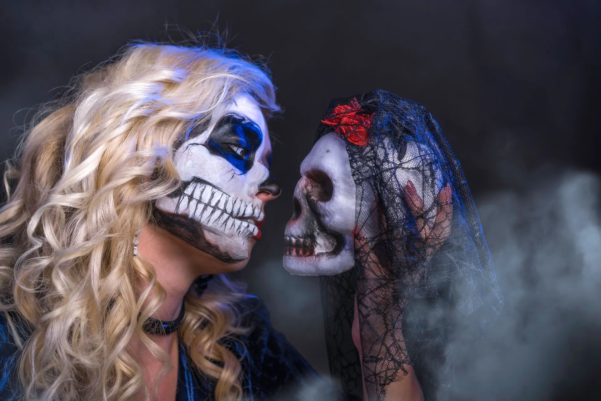 A woman with skull face paint gazes at a veiled skull, creating a spooky Halloween theme.