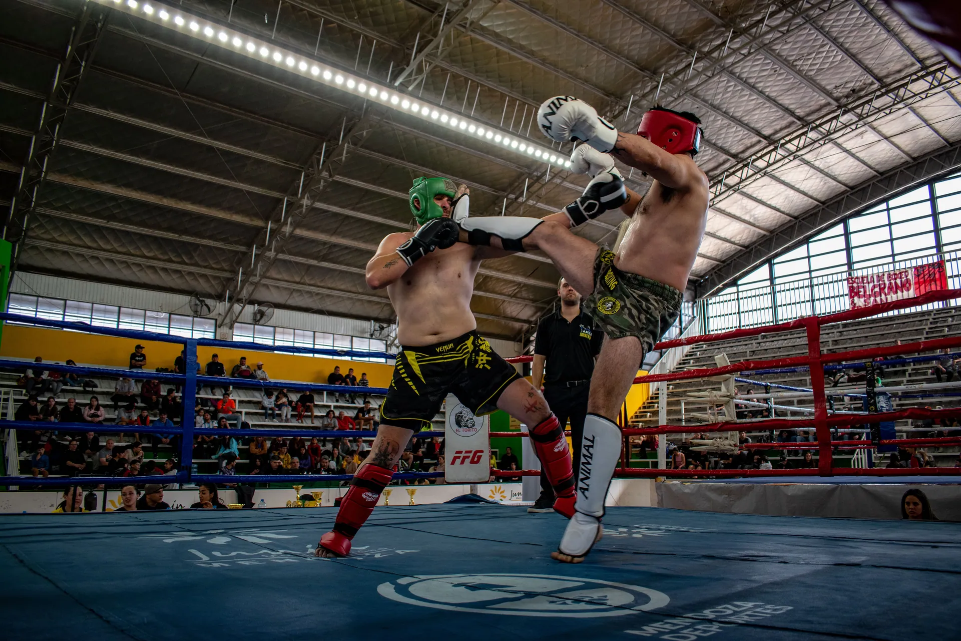 Intense kickboxing match between two male athletes in an indoor arena.