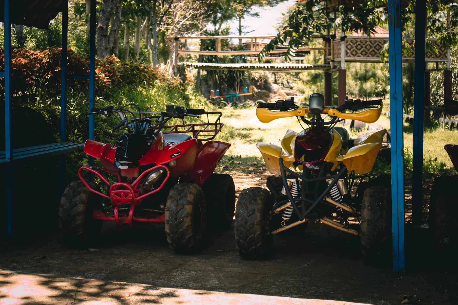 Two quad bikes parked under a shaded area surrounded by lush greenery.