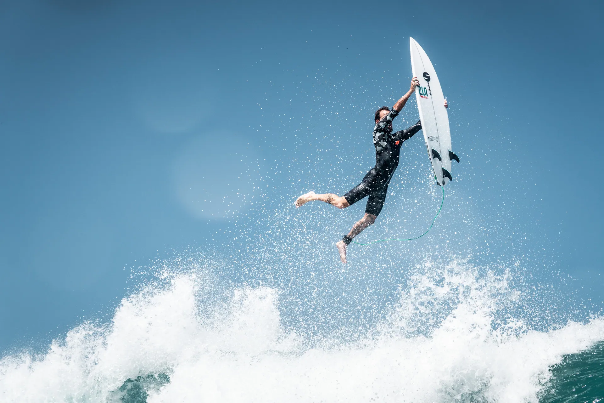 A surfer executes a thrilling leap over a wave, showcasing skill and courage against a clear blue sky.