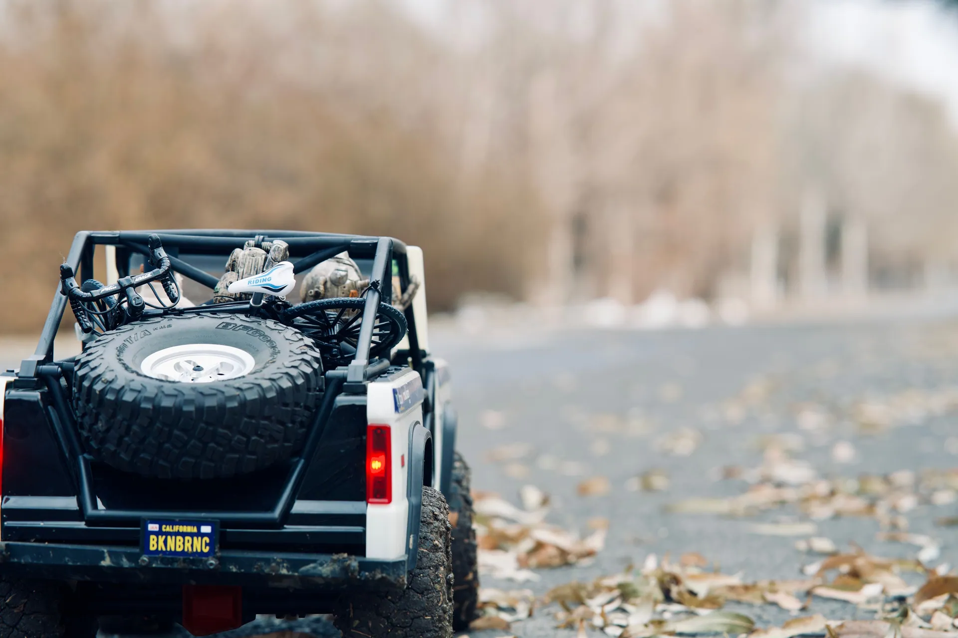 Close-up of a toy SUV model on a leaf-covered forest road, showcasing back view and adventure themes.