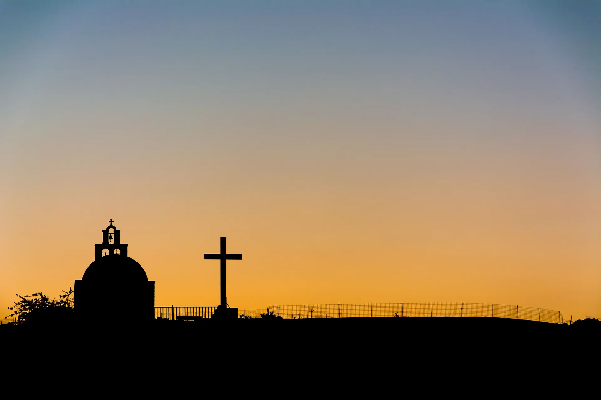 Silhouette of a church and cross against a vibrant orange sunset sky.