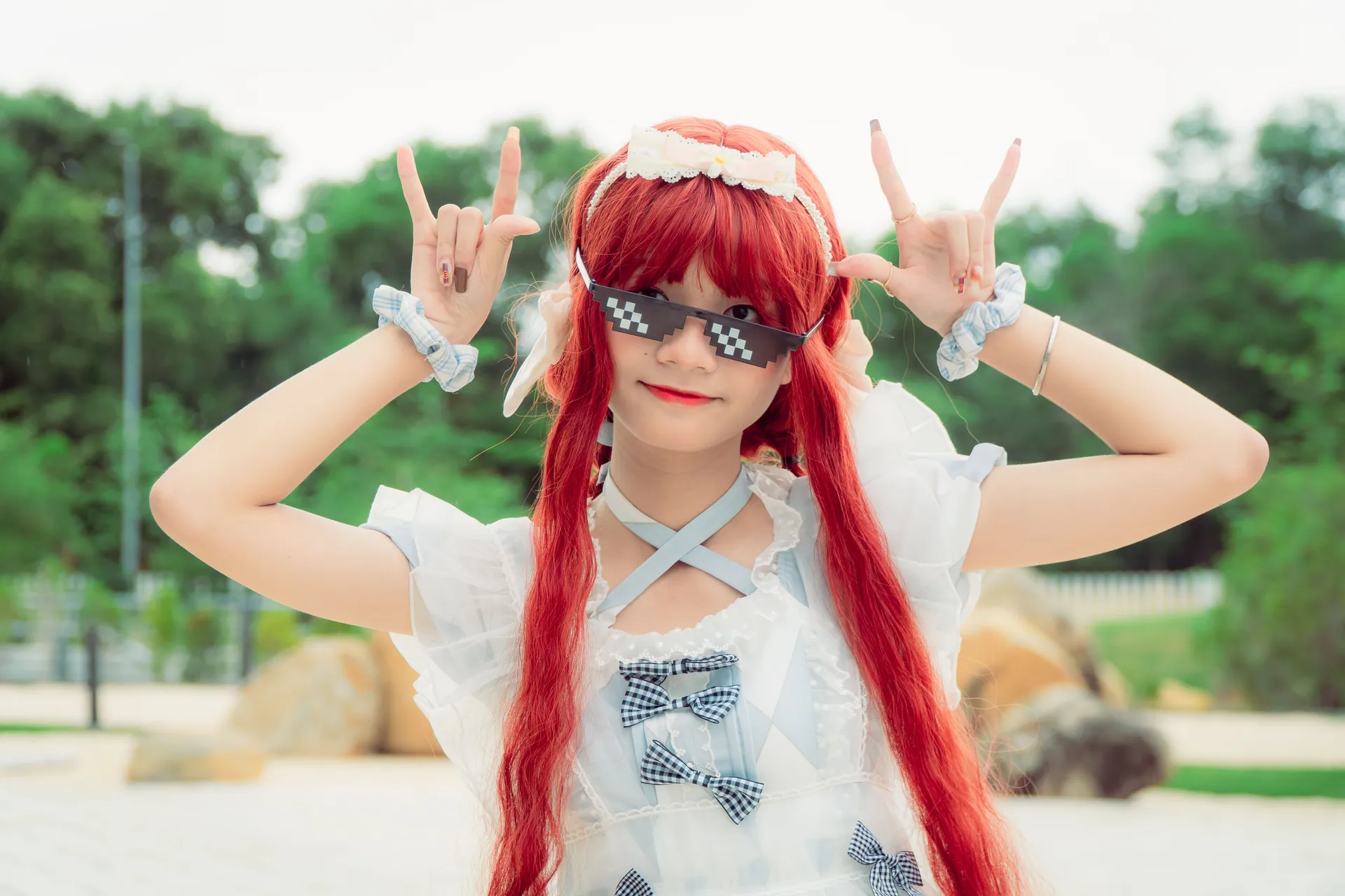 Young woman with red hair and pixel sunglasses in playful cosplay pose outdoors.