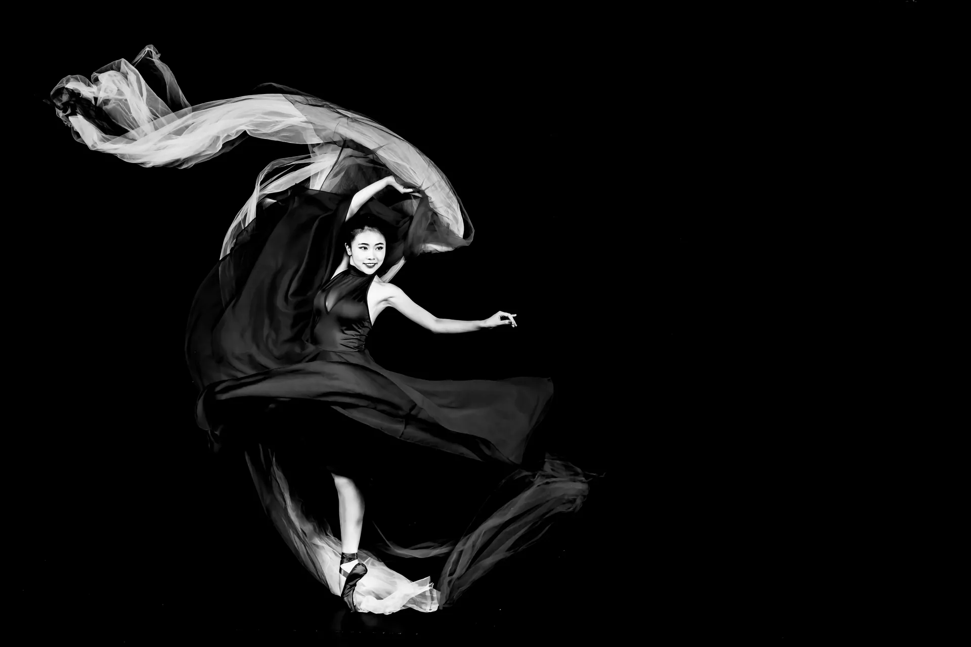 Graceful dancer in a flowing black dress captured mid-motion in black and white.
