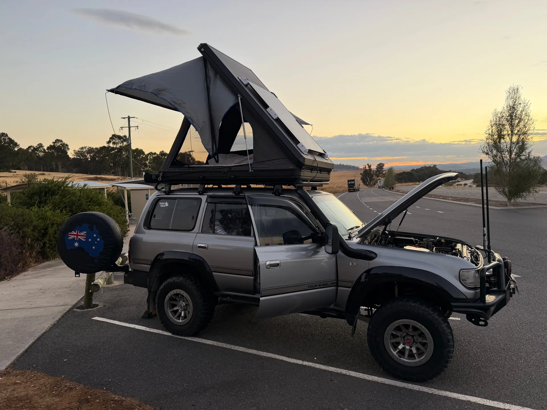 A rugged SUV with rooftop tent set up by the roadside during sunset, perfect for outdoor camping adventures.