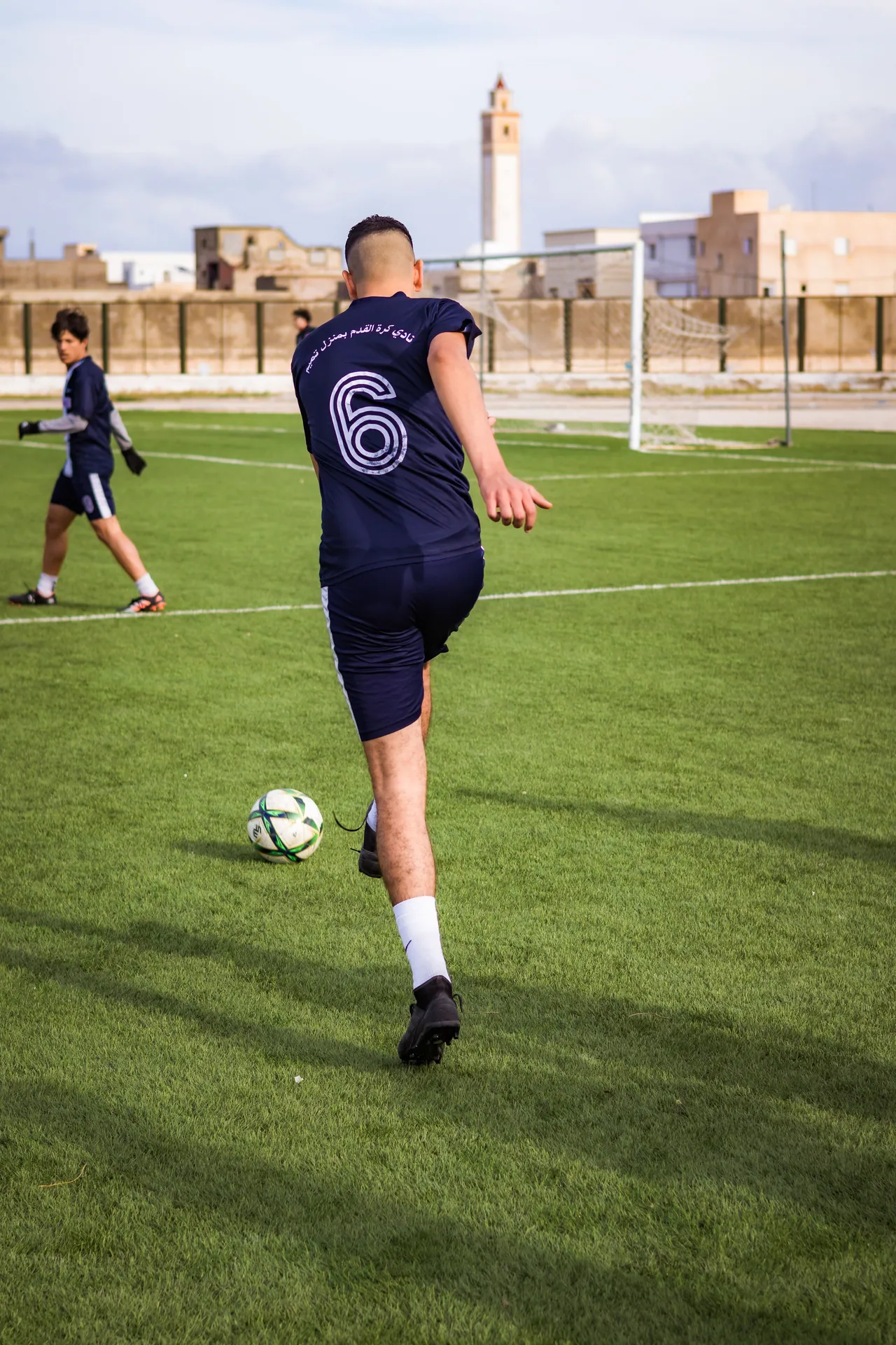A soccer player in sportswear kicks a ball on a grass field during daytime practice.