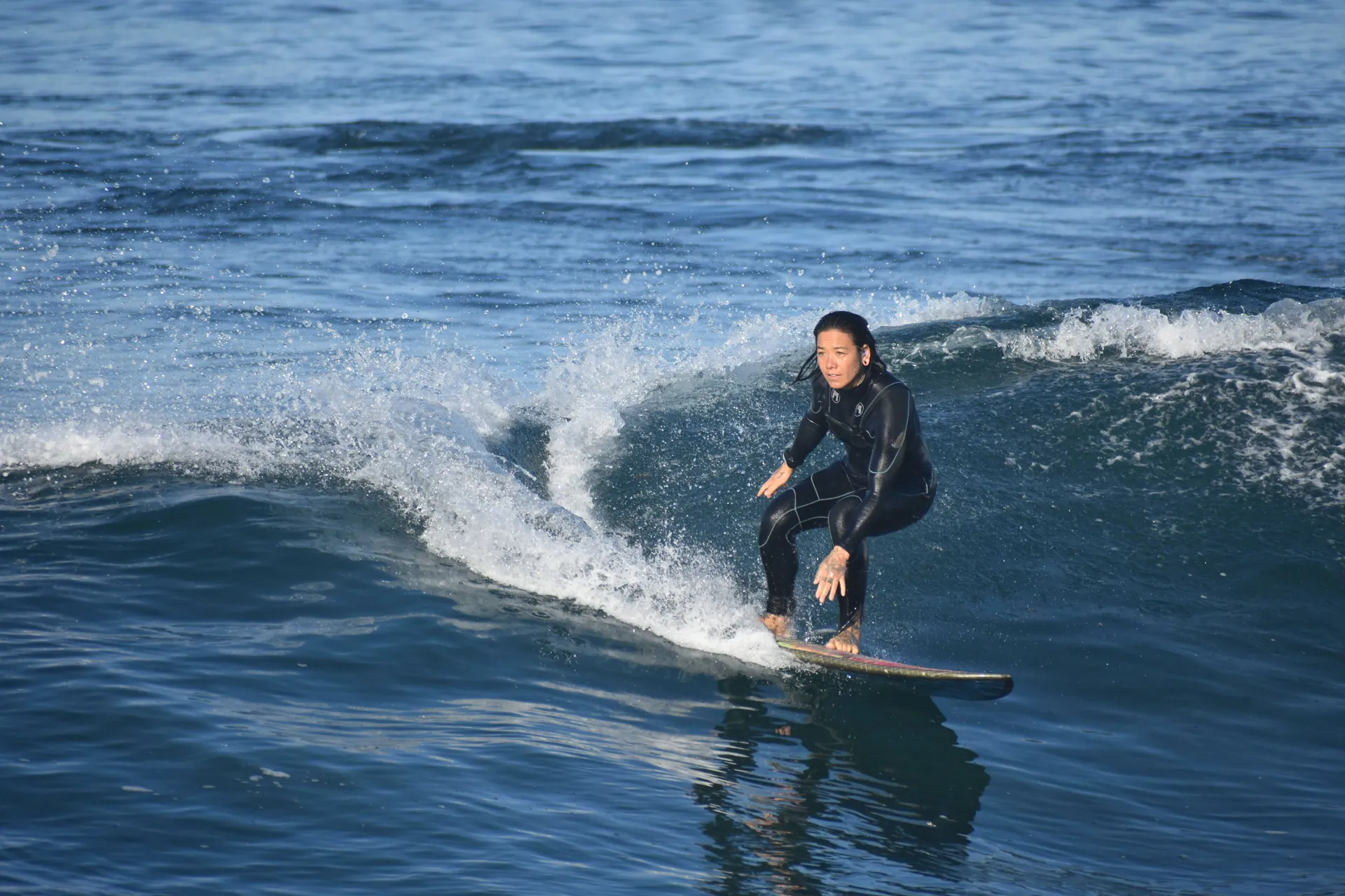 An adult surfer in a wetsuit skillfully rides a wave during the day, showcasing surfing skills.