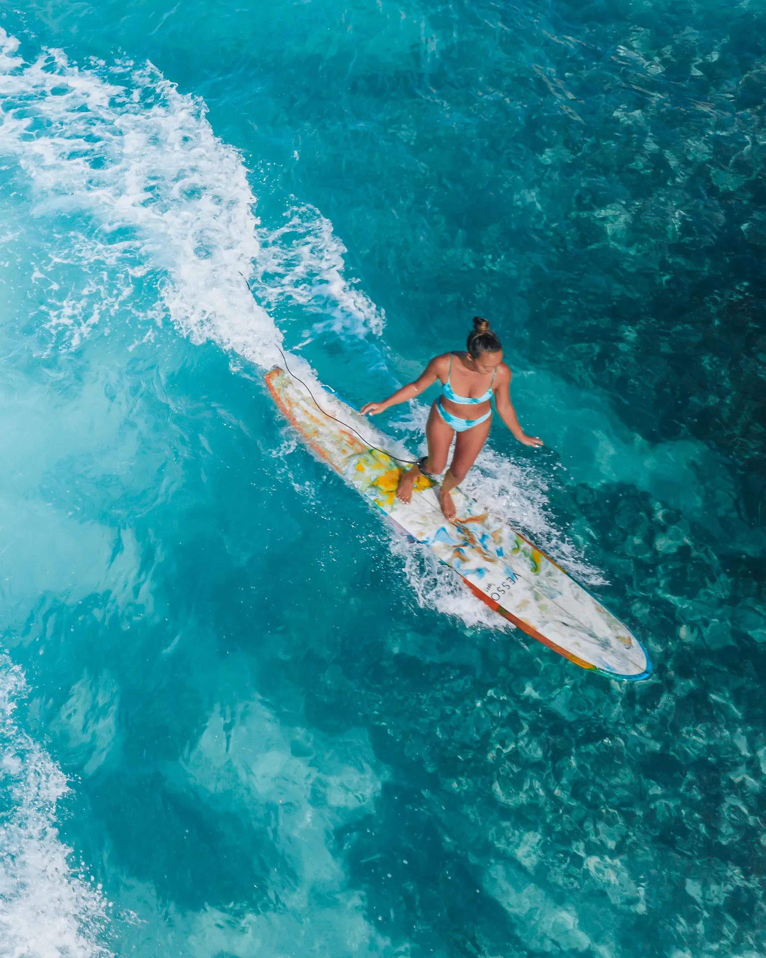 Aerial shot of a woman surfing on vibrant turquoise ocean waves, capturing the thrill of water sports.