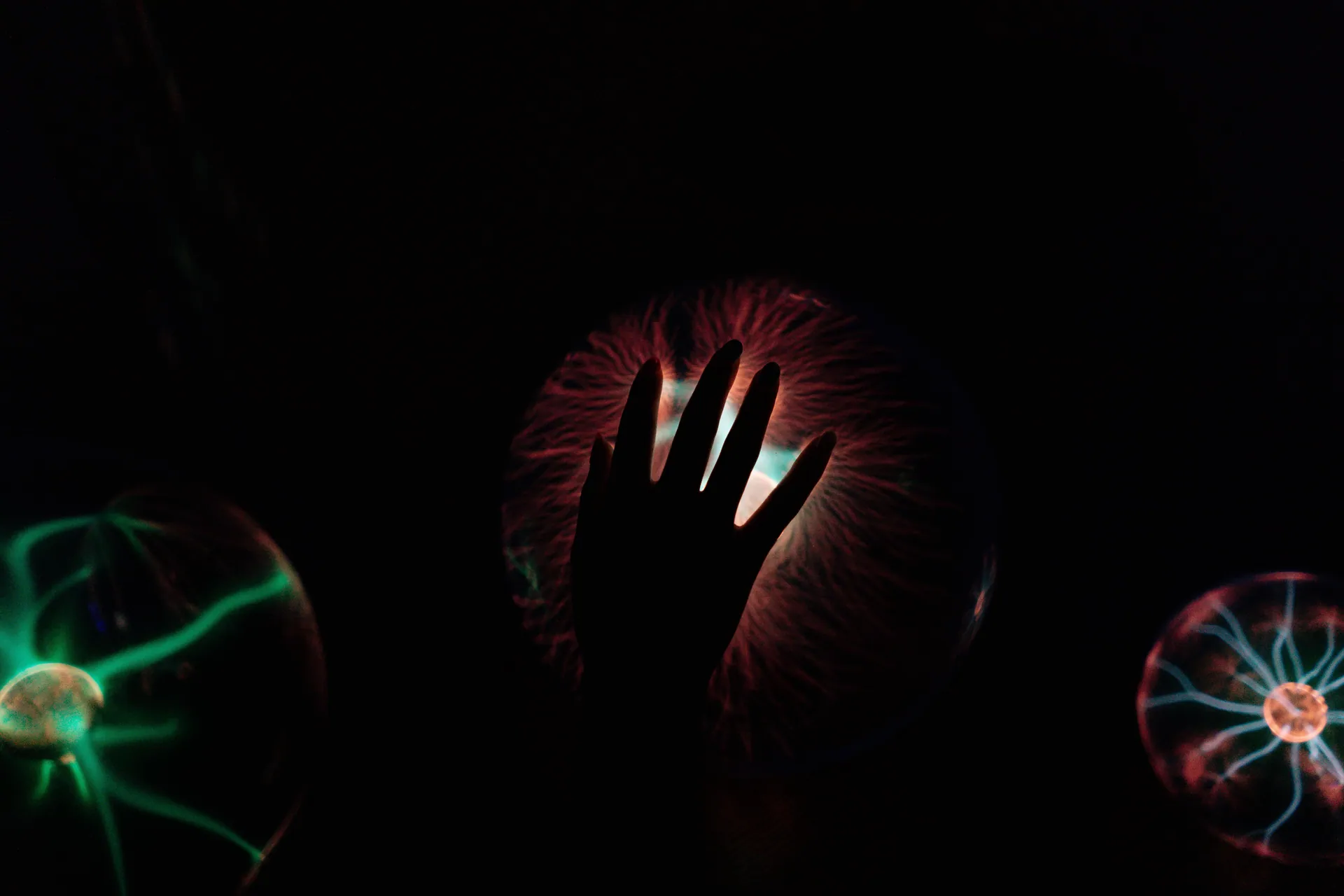 Silhouette of a hand interacting with a glowing plasma ball, illustrating electric waves.