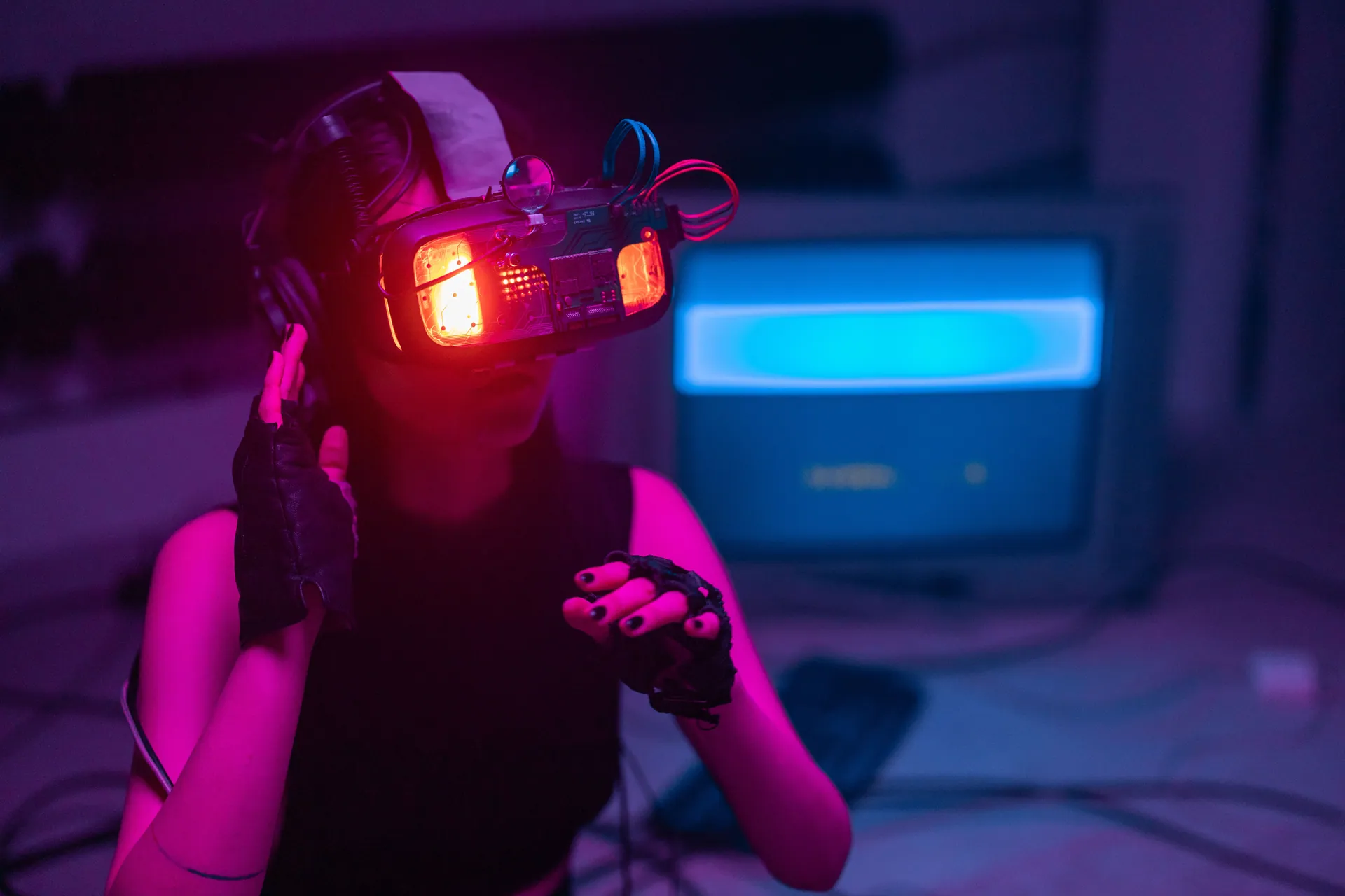 A woman immerses in virtual reality with neon-lit goggles and gloves in a tech-savvy environment.