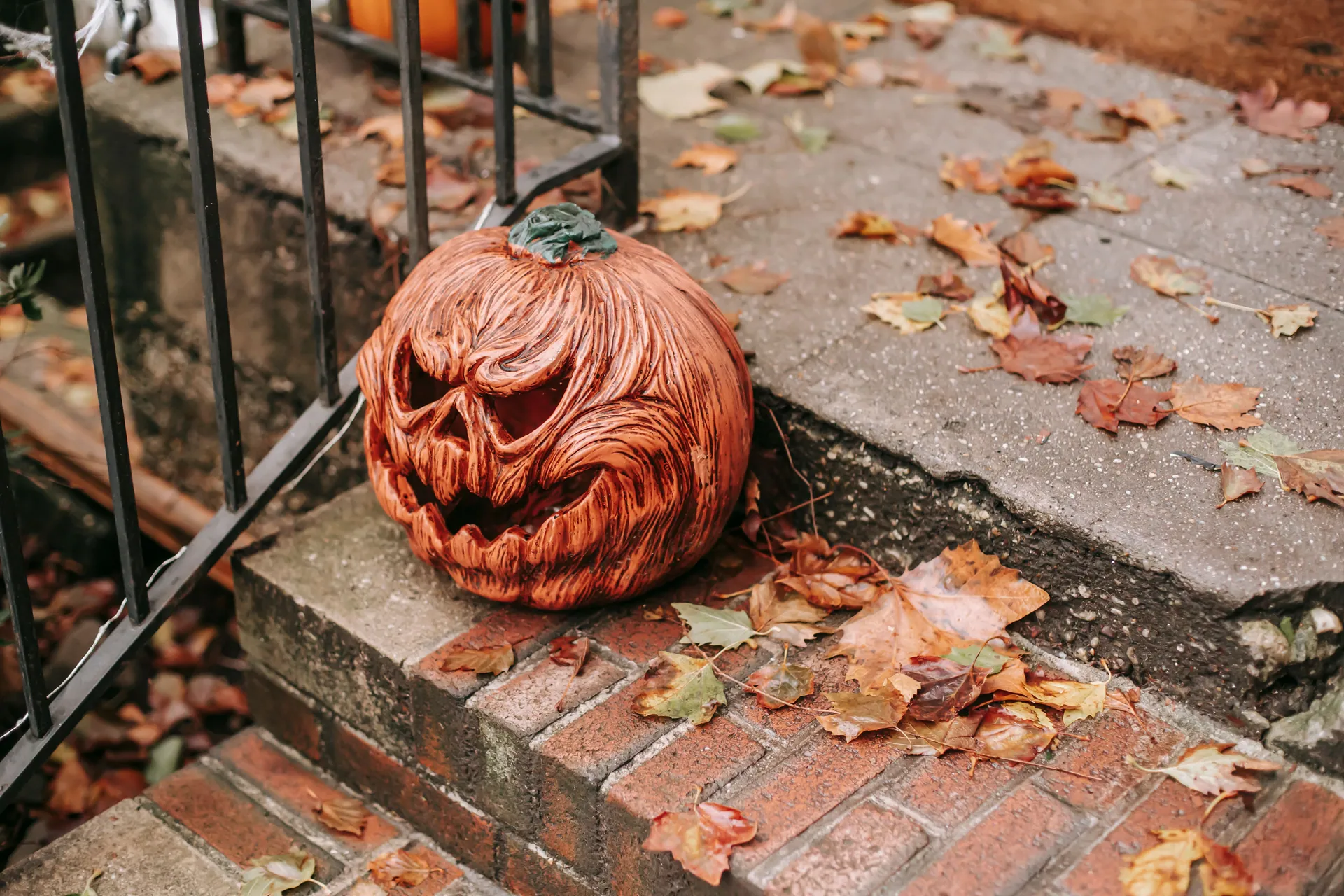 Creepy orange pumpkin placed on stairs near house with metal railing in autumn day on Halloween