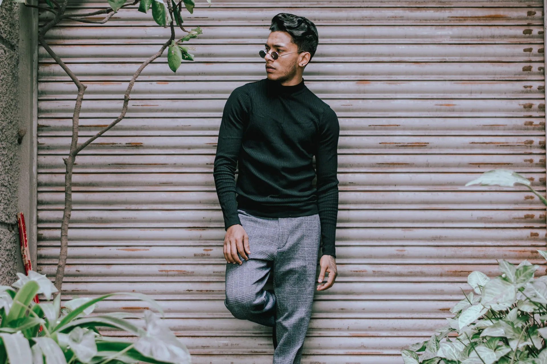 Fashionable young man in sunglasses posing confidently outdoors against metal shutter.