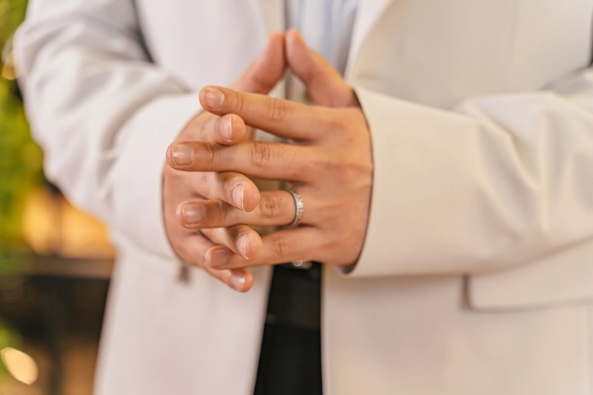 A close-up of hands clasped showing a ring and white suit details.