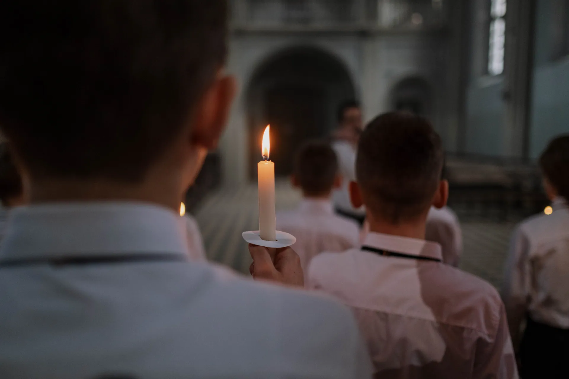 Boys in a church choir hold candles during a rehearsal, creating a warm and religious atmosphere.